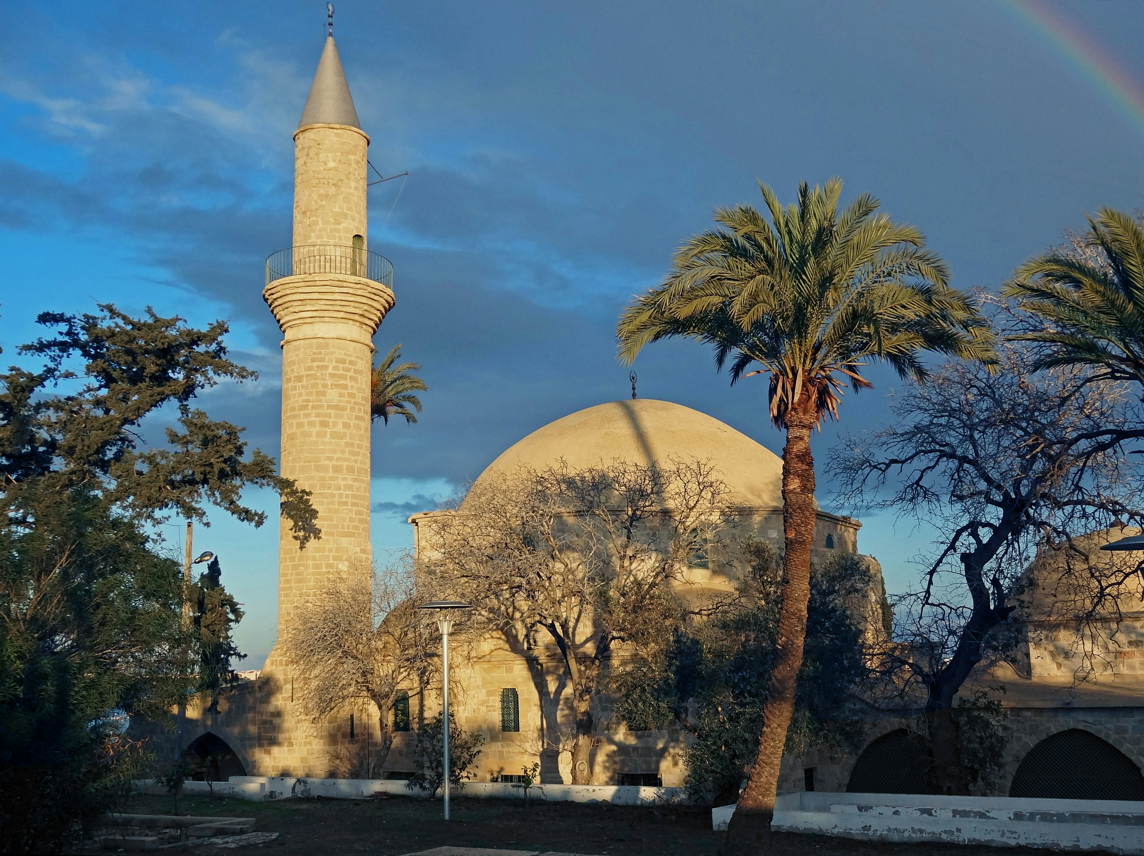 Scenic view of a mosque with a dome and minaret under a blue sky and rainbow