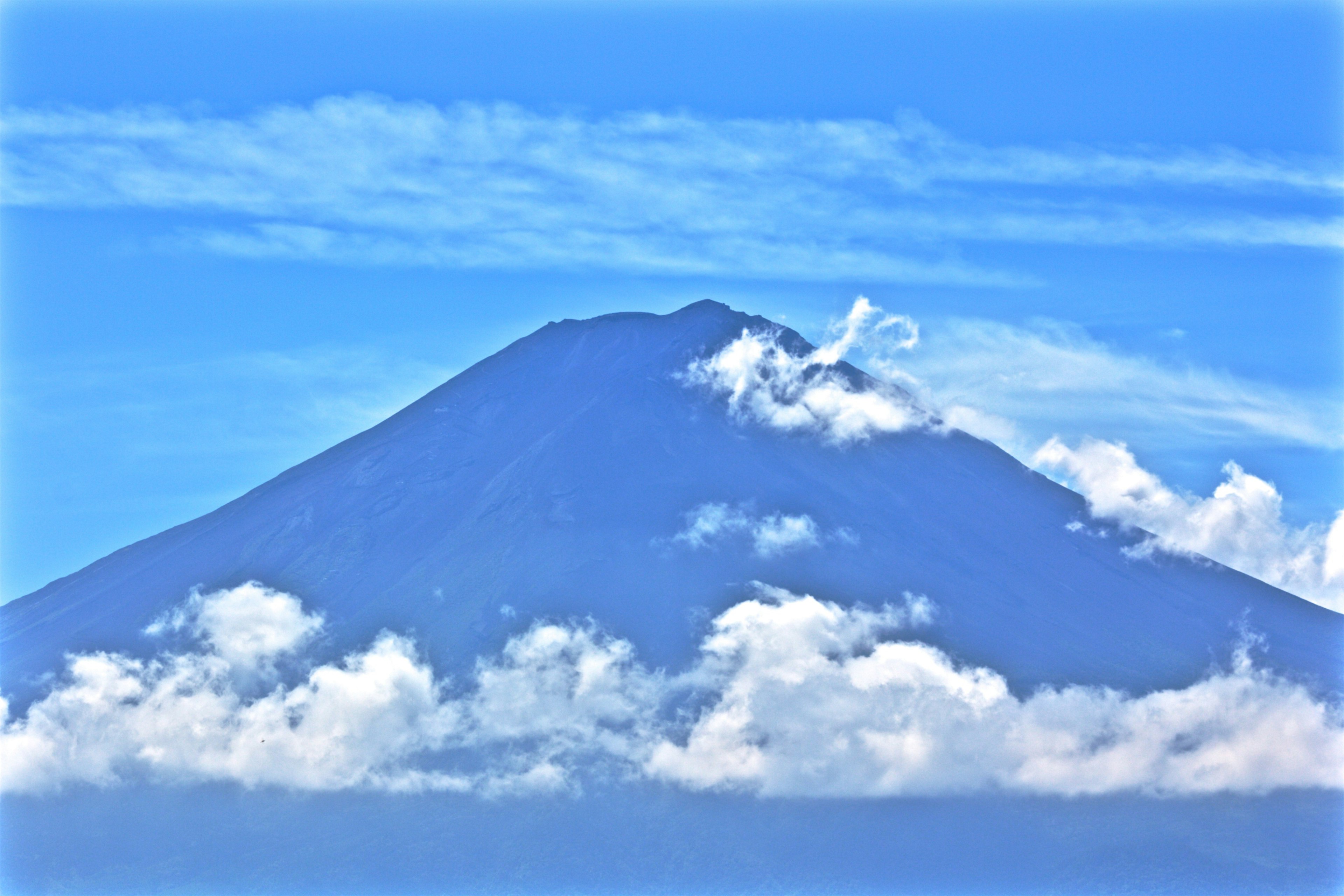 Sebuah gunung indah dikelilingi awan di bawah langit biru