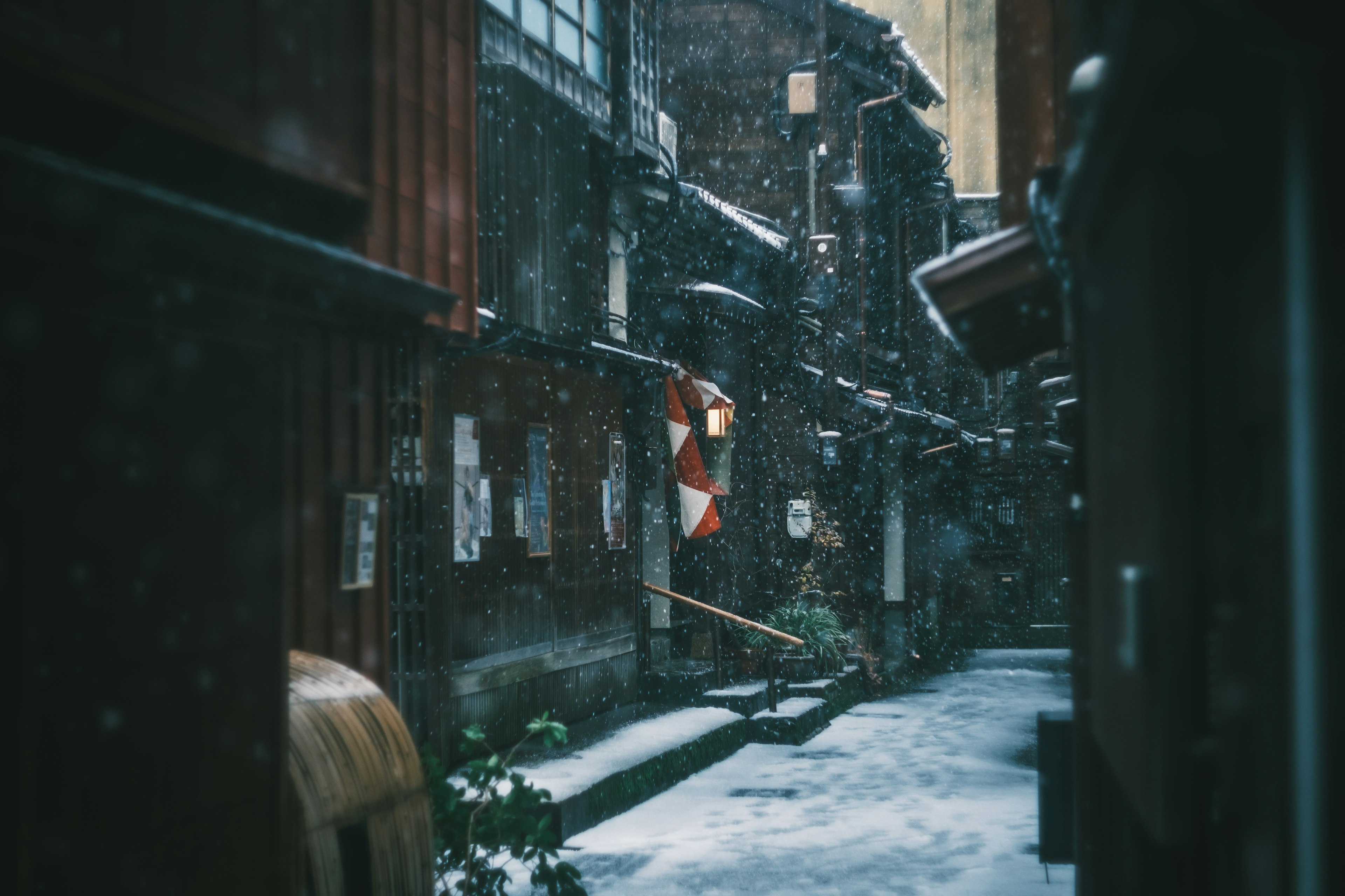 Narrow alley with old buildings and a red and white lantern in the snowfall