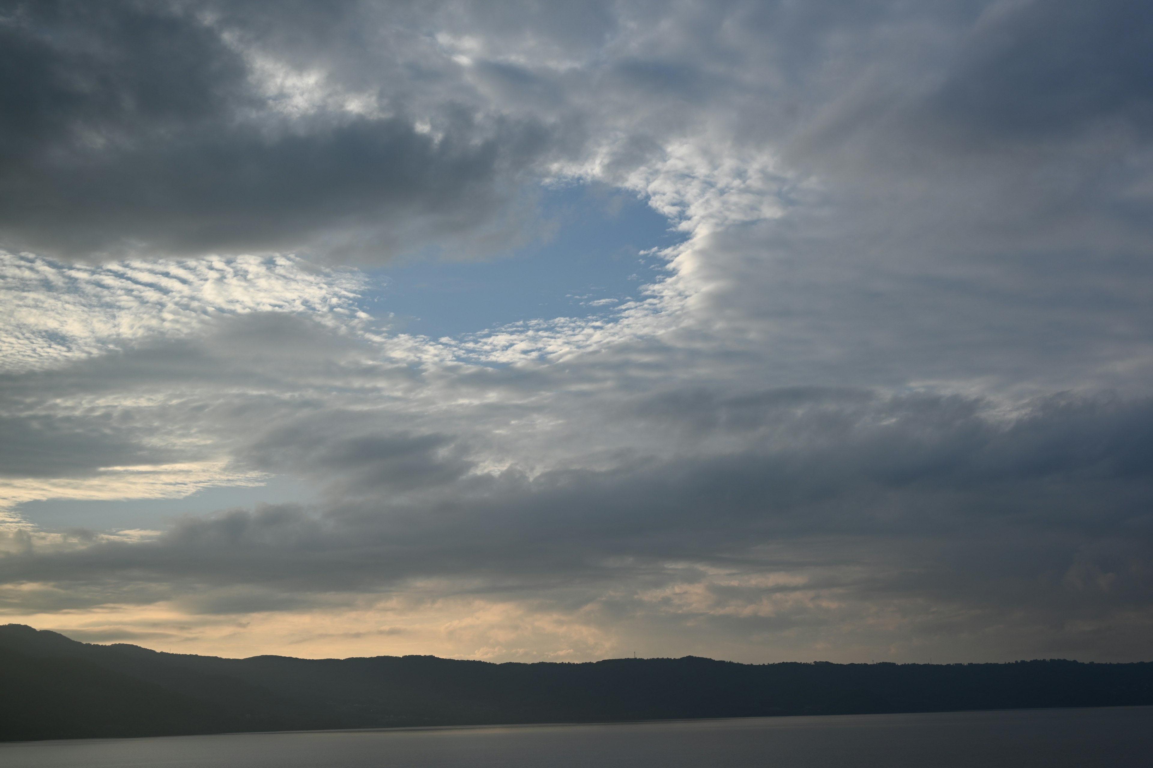 A landscape showing blue sky peeking through clouds over a lake