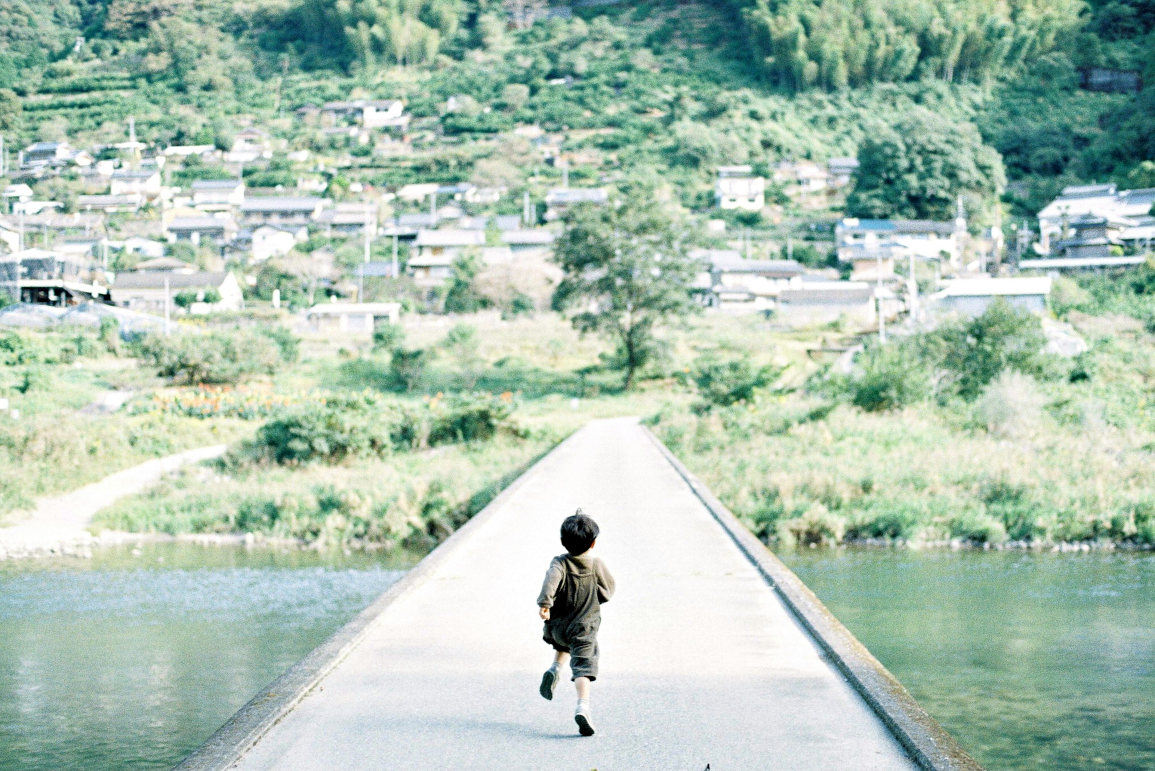 A child running on a bridge with green mountains and a village in the background