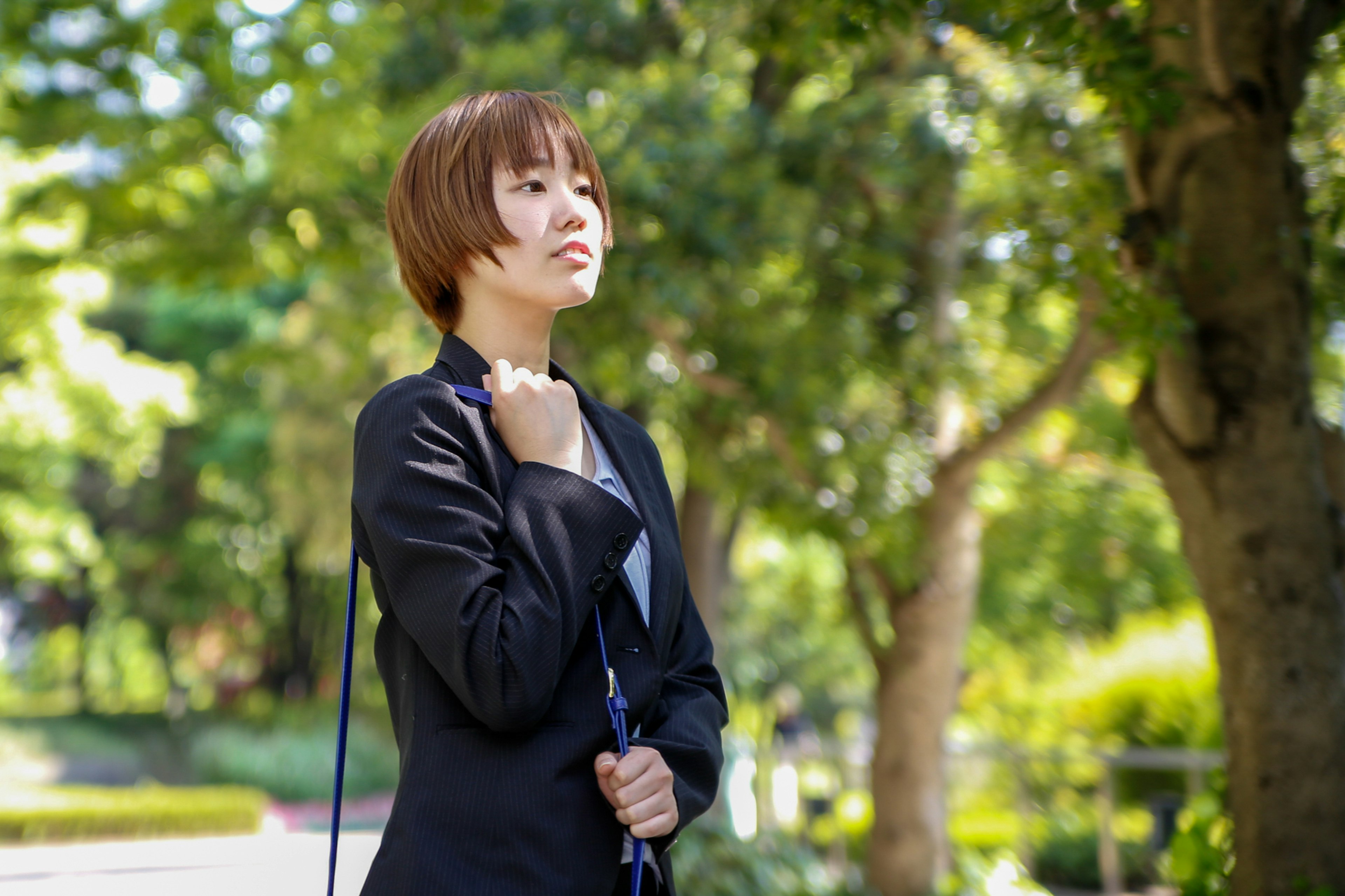 Side profile of a woman holding an umbrella in a park with green trees in the background