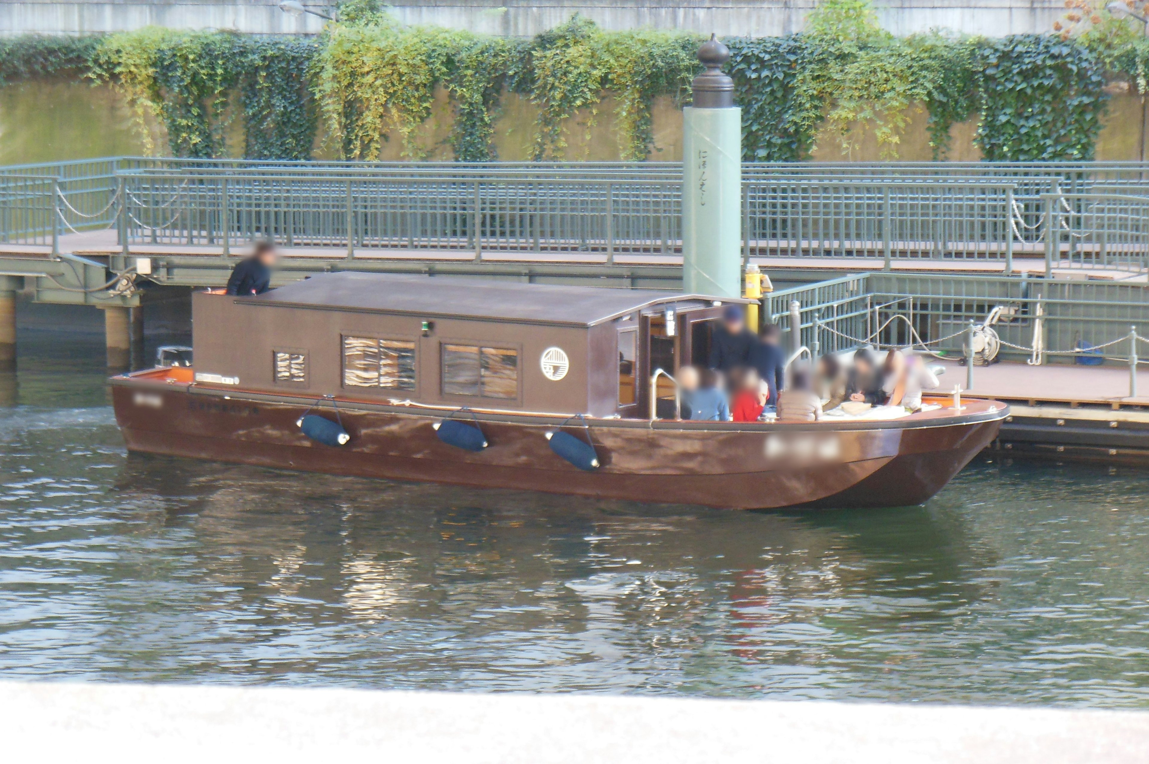 Una barca marrone ormeggiata in un fiume con persone a bordo