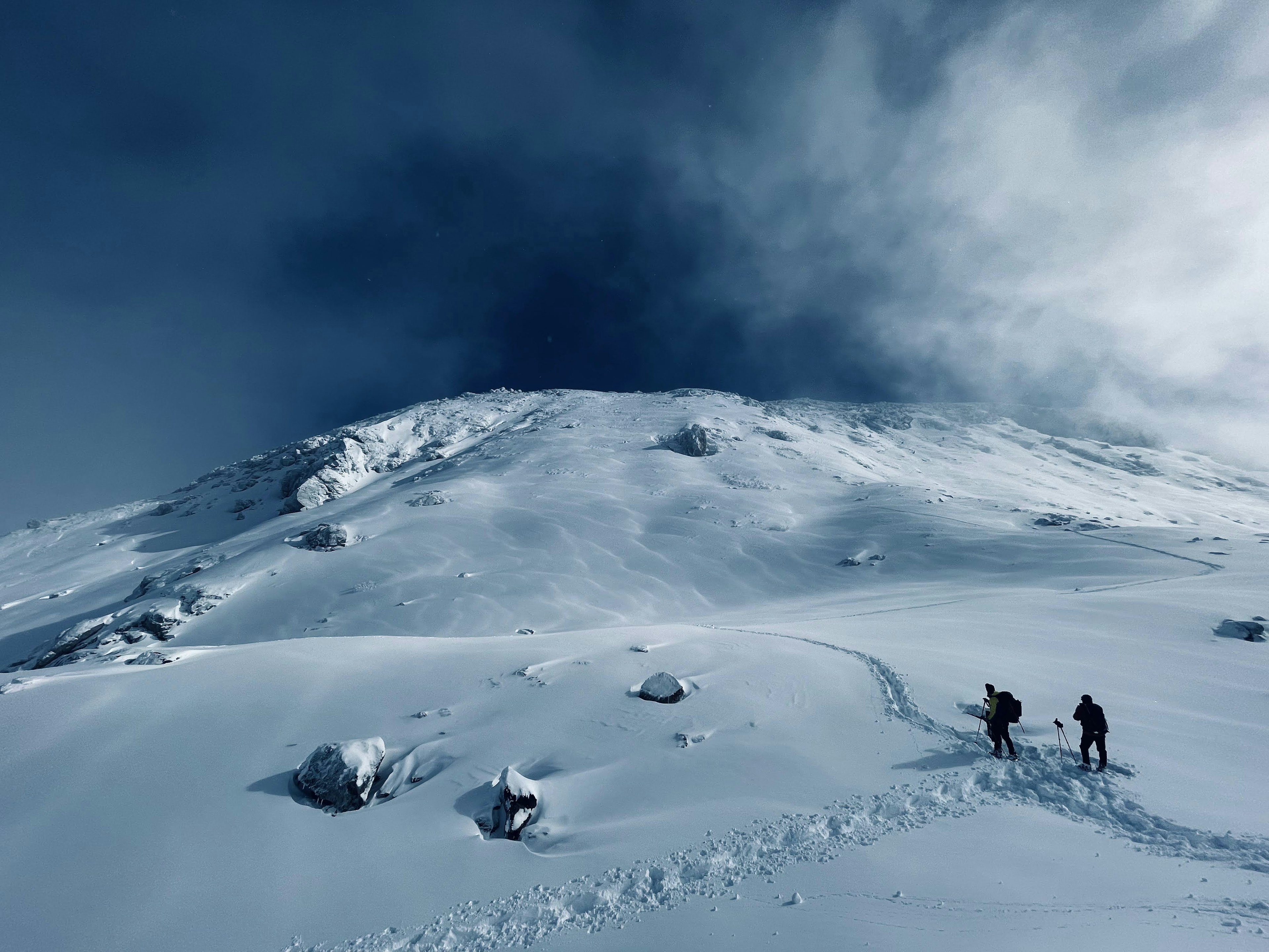 Silhouette of two climbers ascending a snow-covered mountain