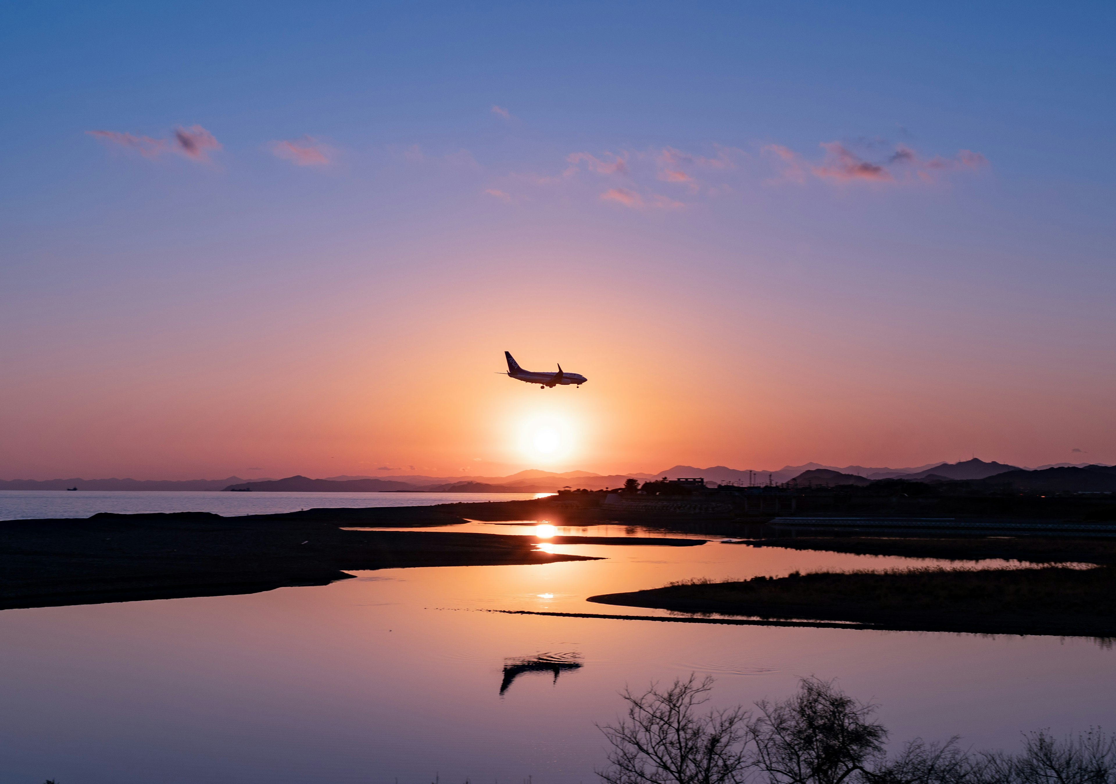 Flugzeug fliegt vor einem Sonnenuntergang über ruhigem Wasser