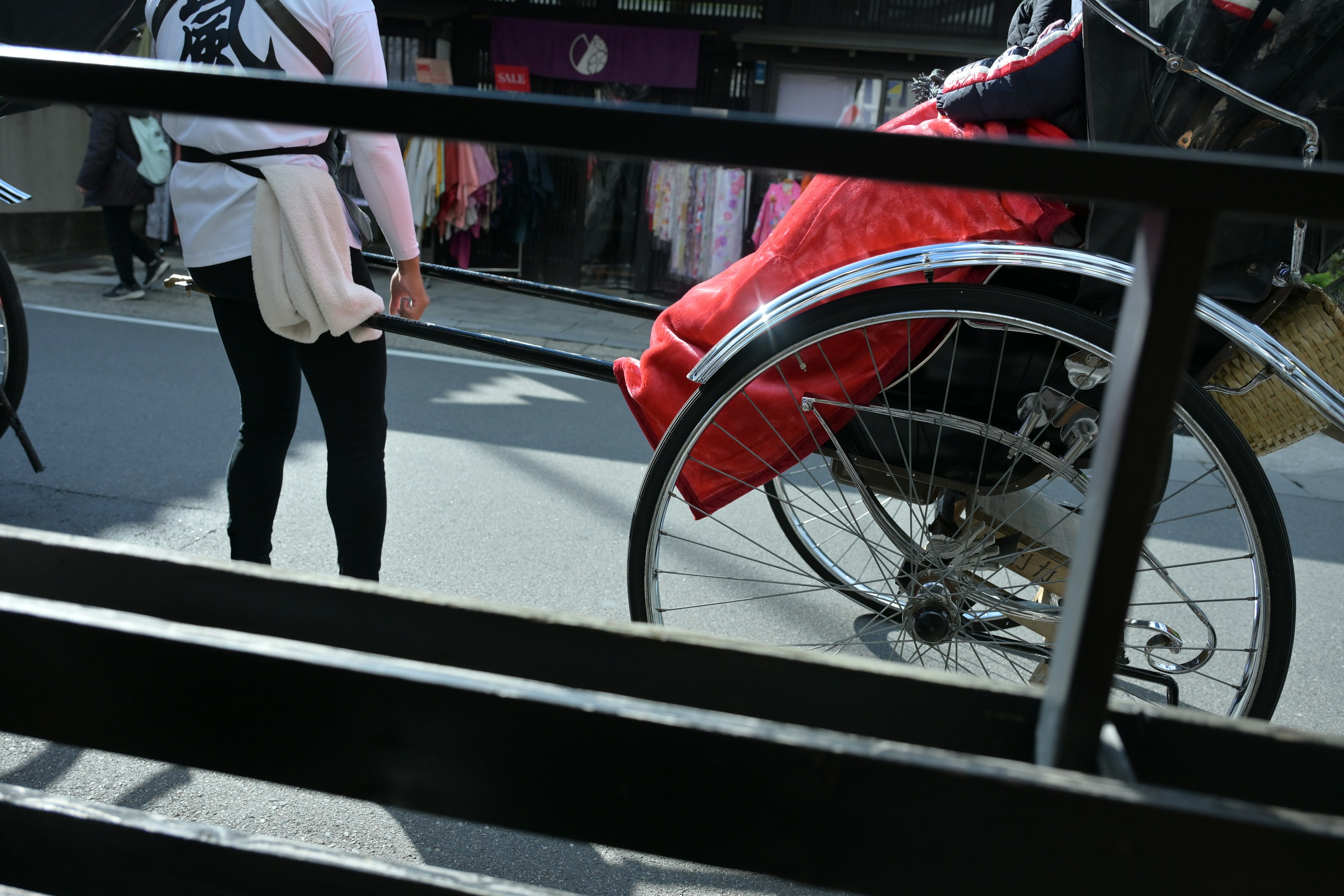 人力車の横に立つ人と赤い布が見える街の風景