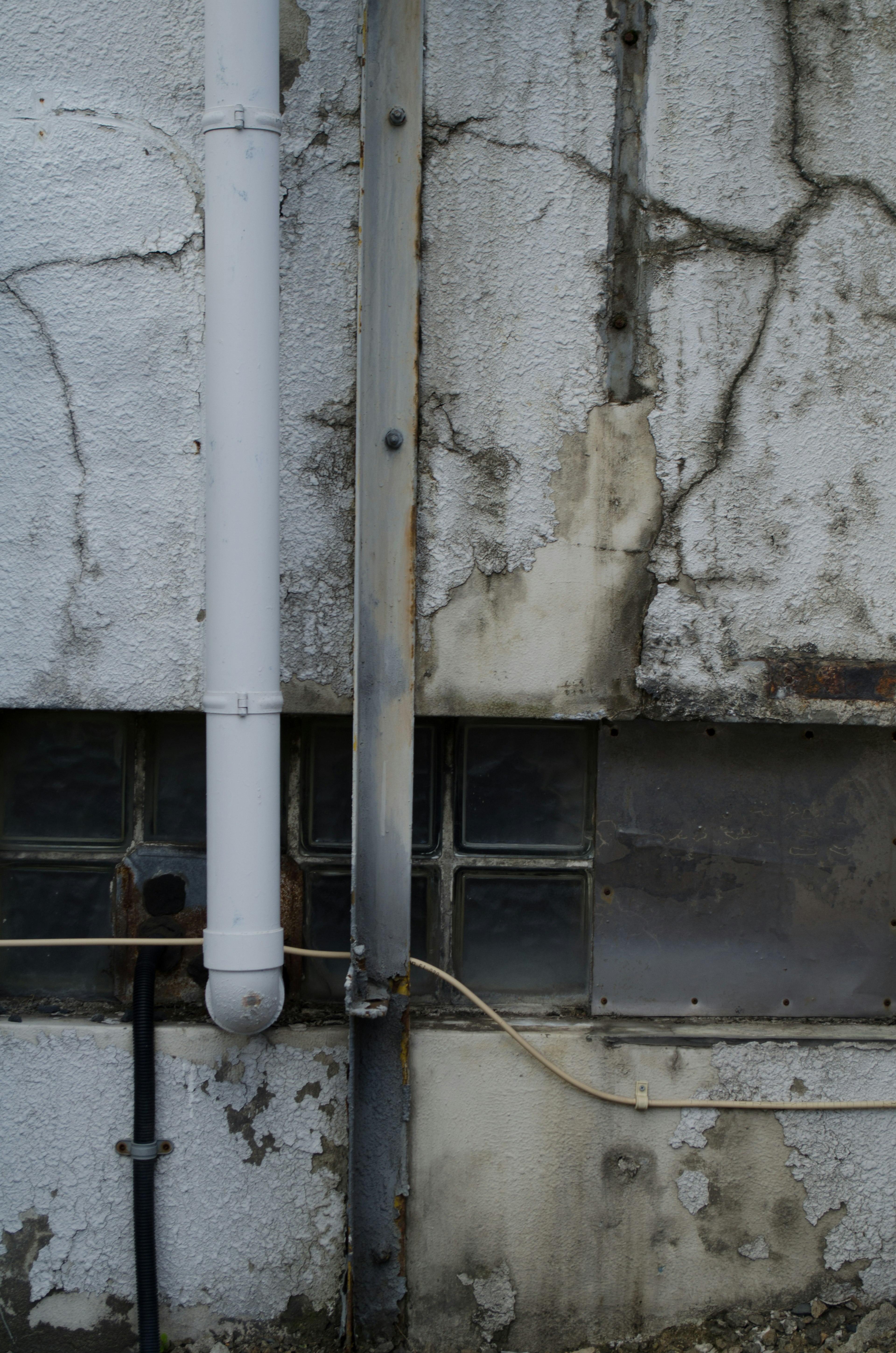 Section of an old building featuring a cracked wall and a white pipe