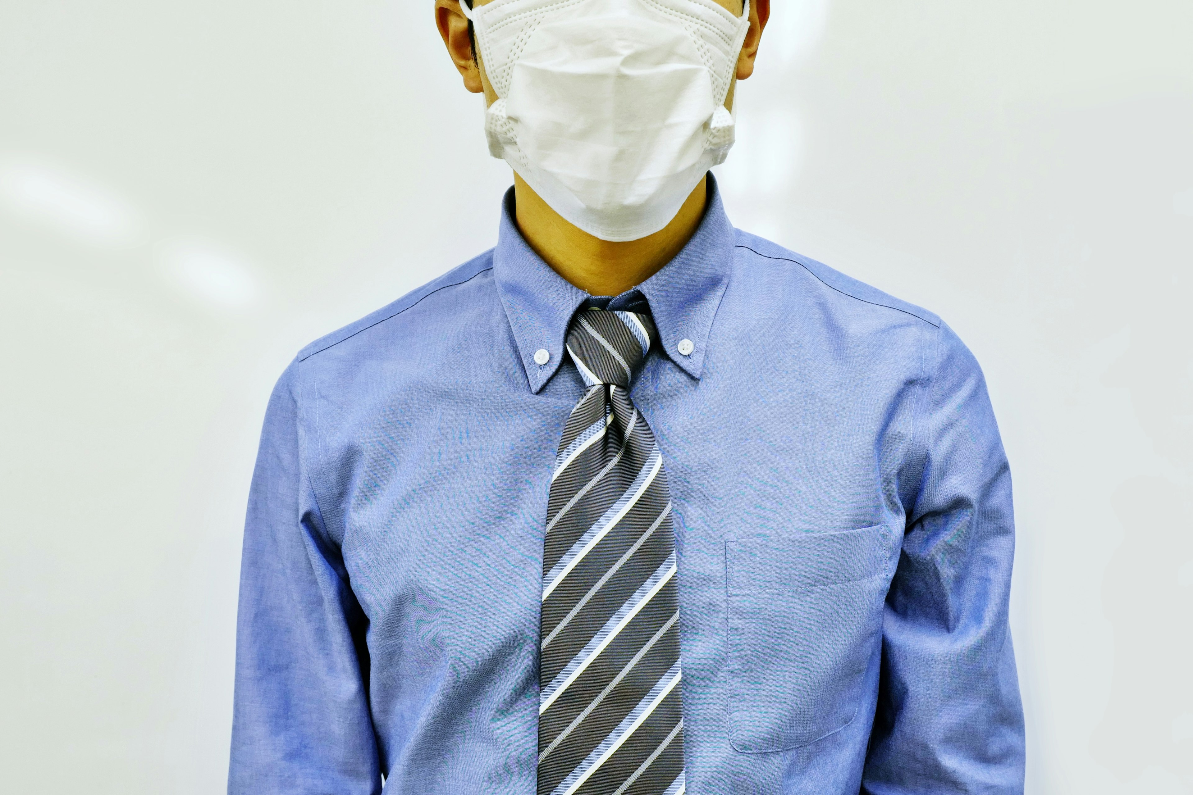 A man wearing a mask with a blue shirt and striped tie