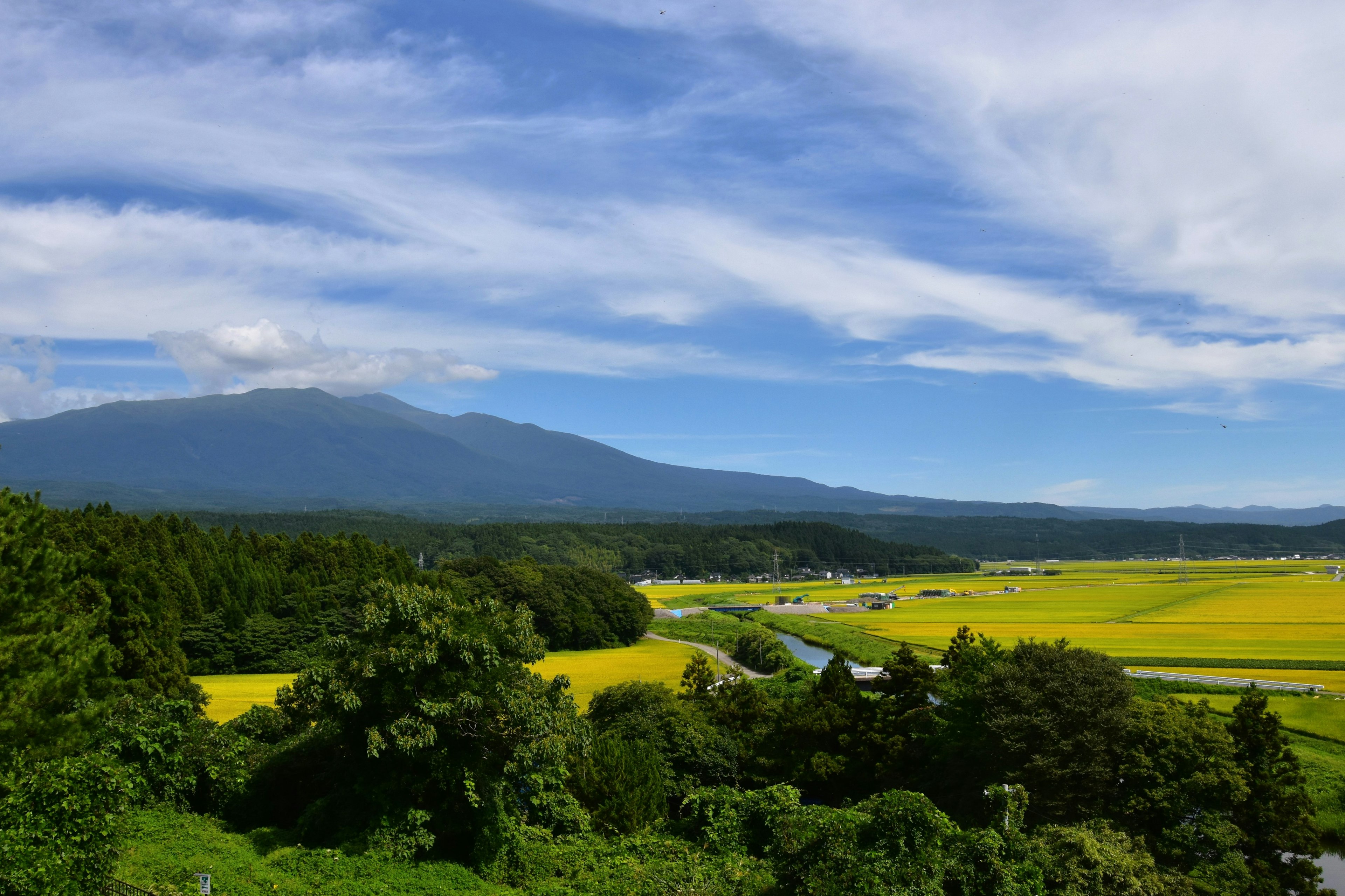 Pemandangan pegunungan dengan langit biru dan awan putih di atas ladang hijau