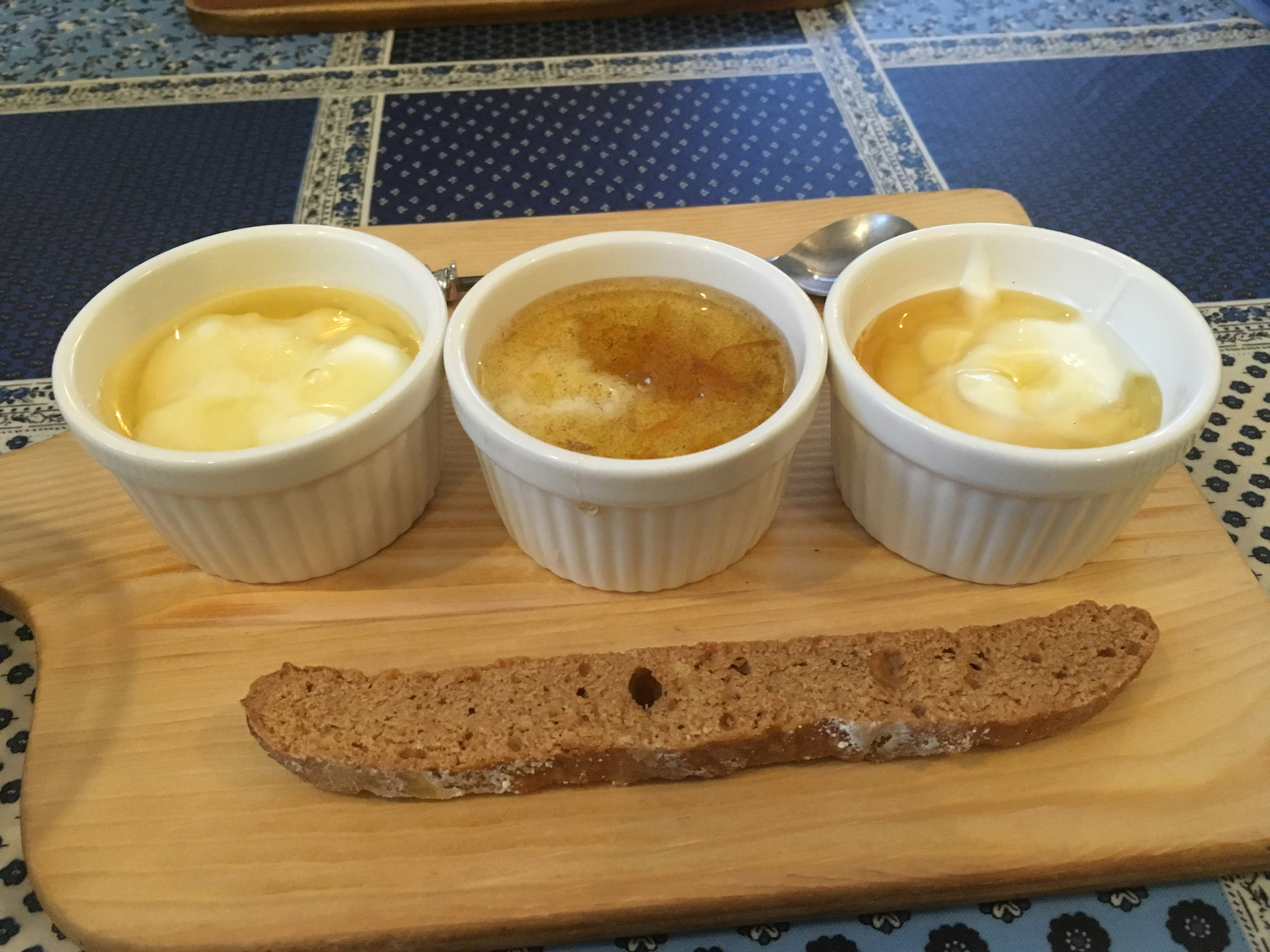 Three small white cups filled with desserts on a wooden board with a biscuit