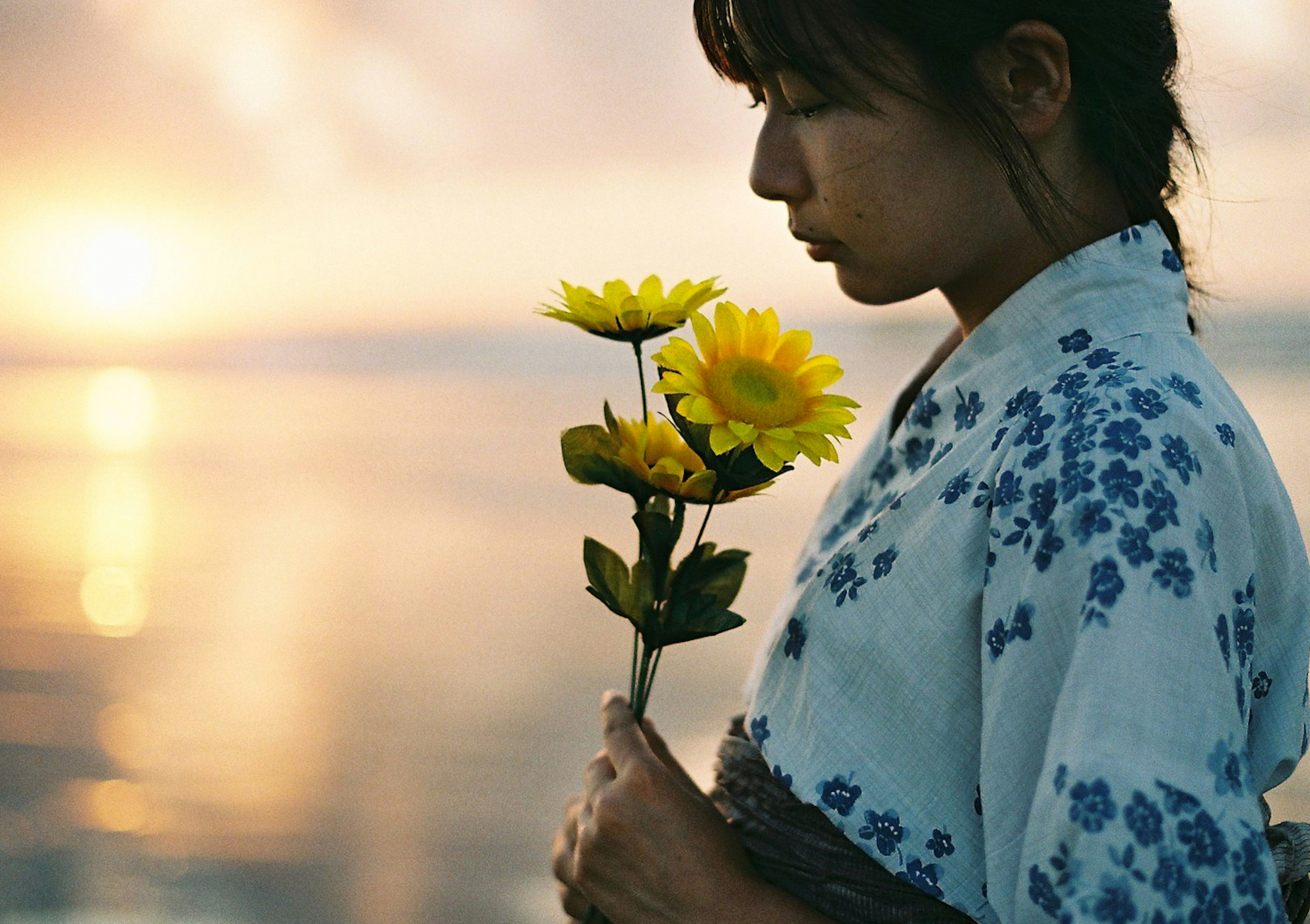 夕焼けを背景にした和服の女性がひまわりを持つ