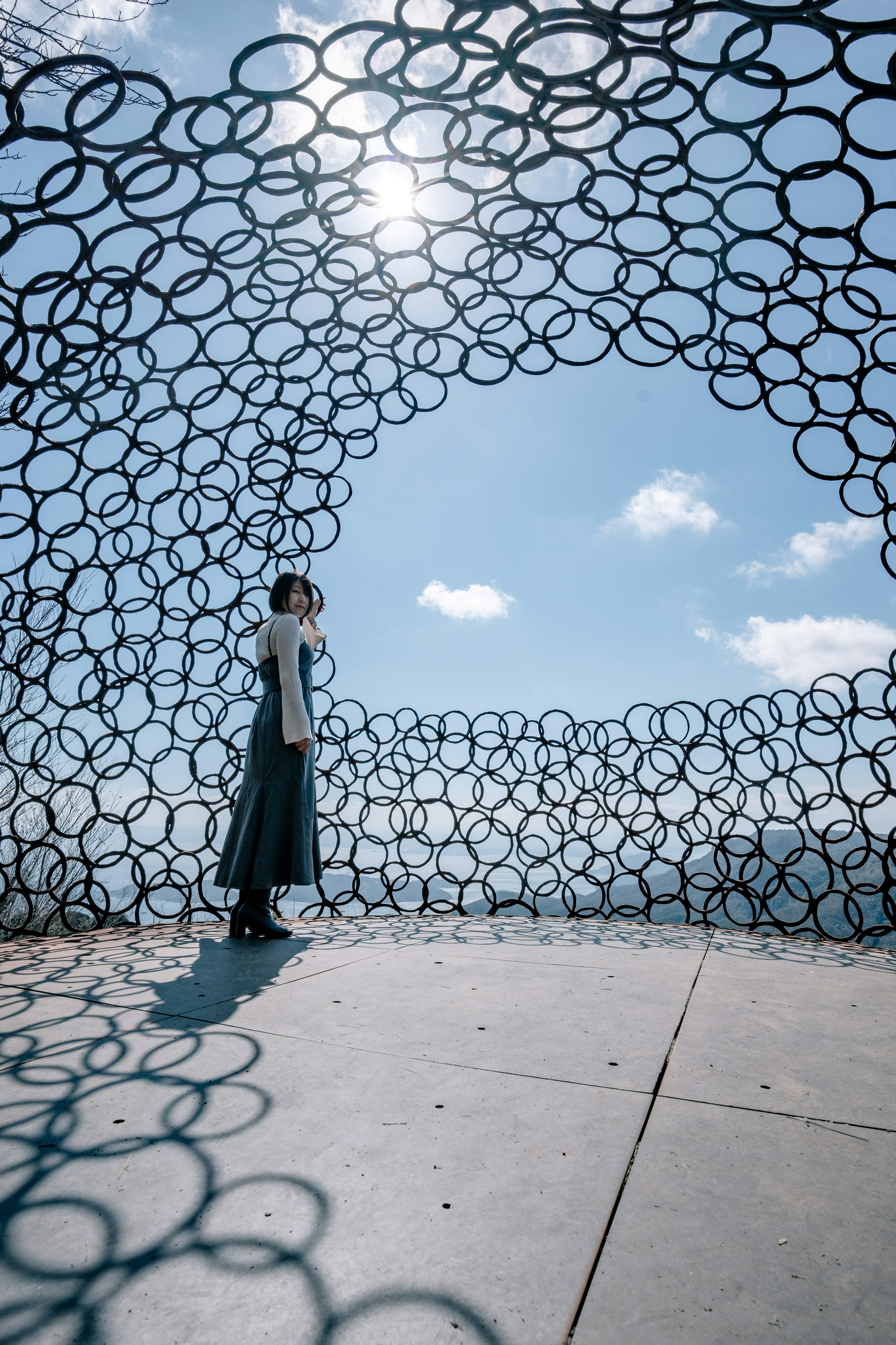 A woman standing inside a circular metal ring structure under a blue sky