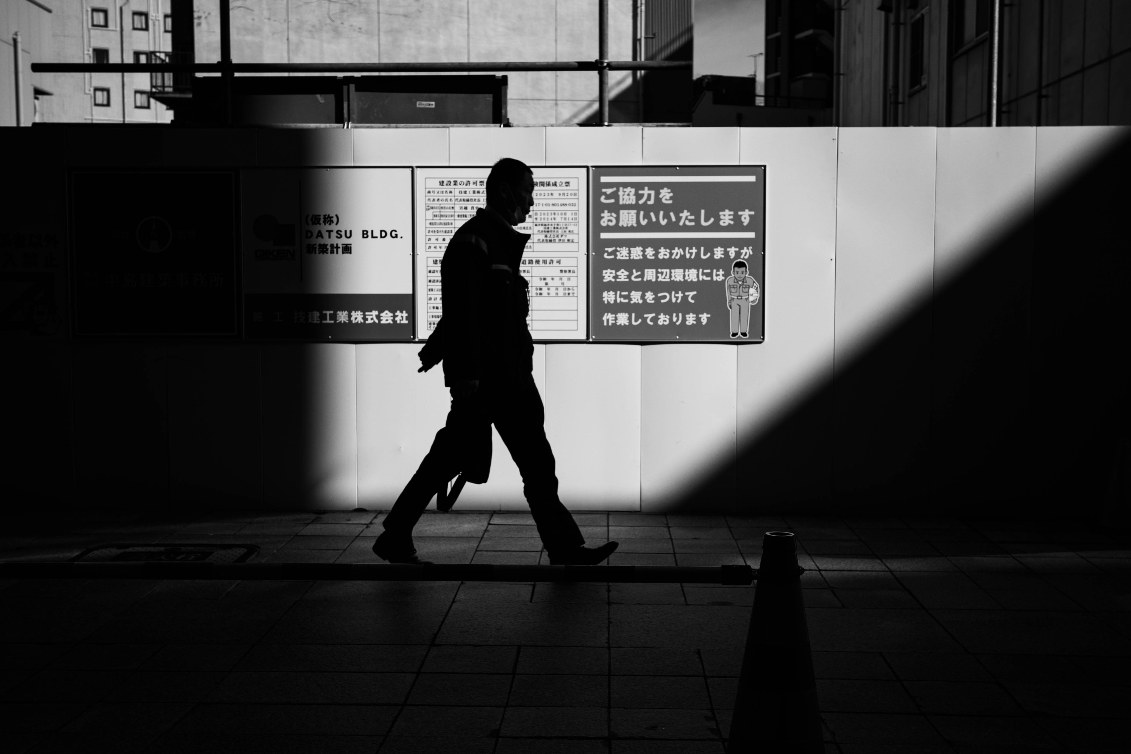 Une image en noir et blanc à fort contraste d'une silhouette marchant devant des panneaux