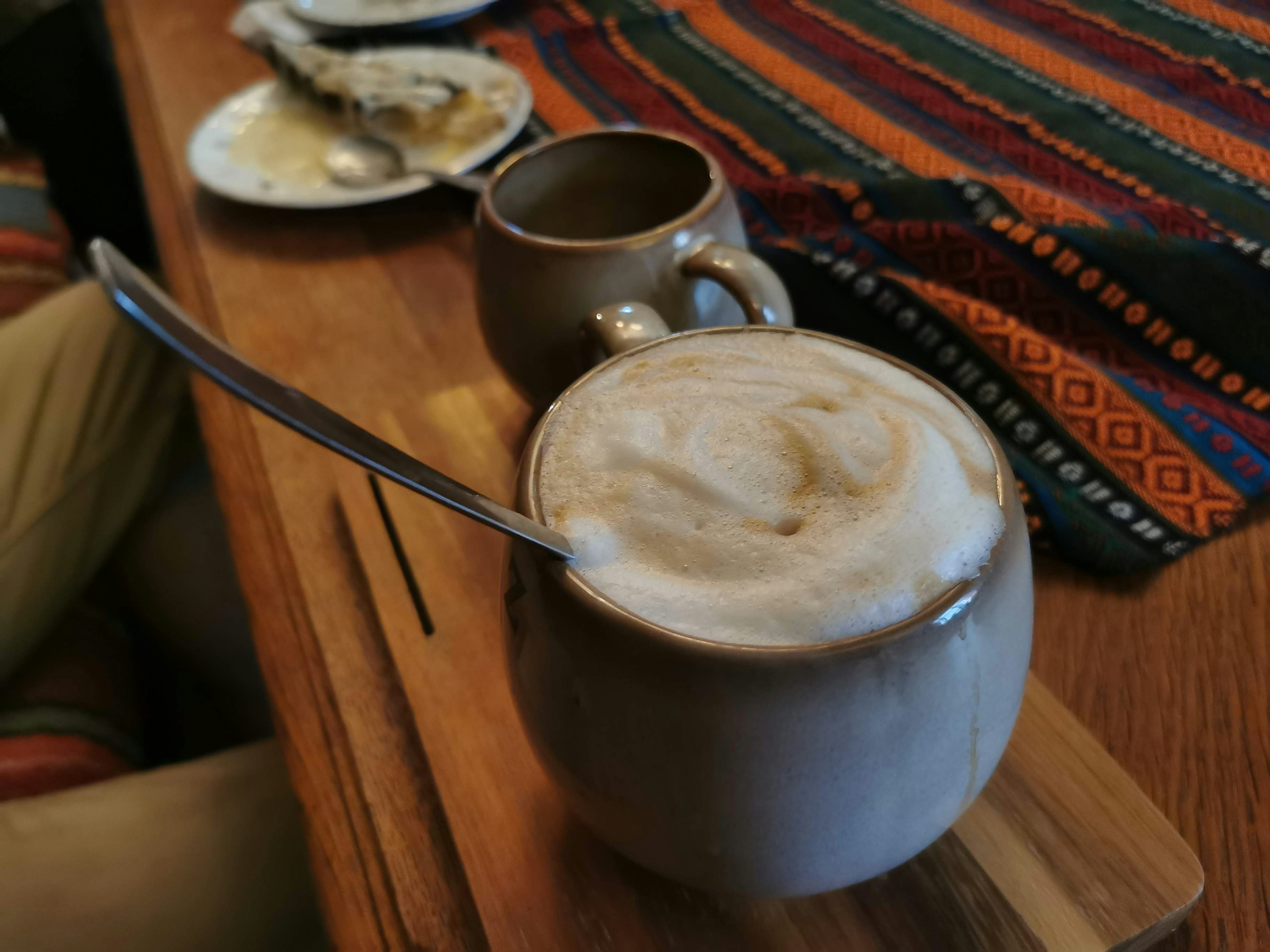 Secangkir latte lezat dalam cangkir keramik dengan cangkir kecil di dekatnya di atas meja kayu