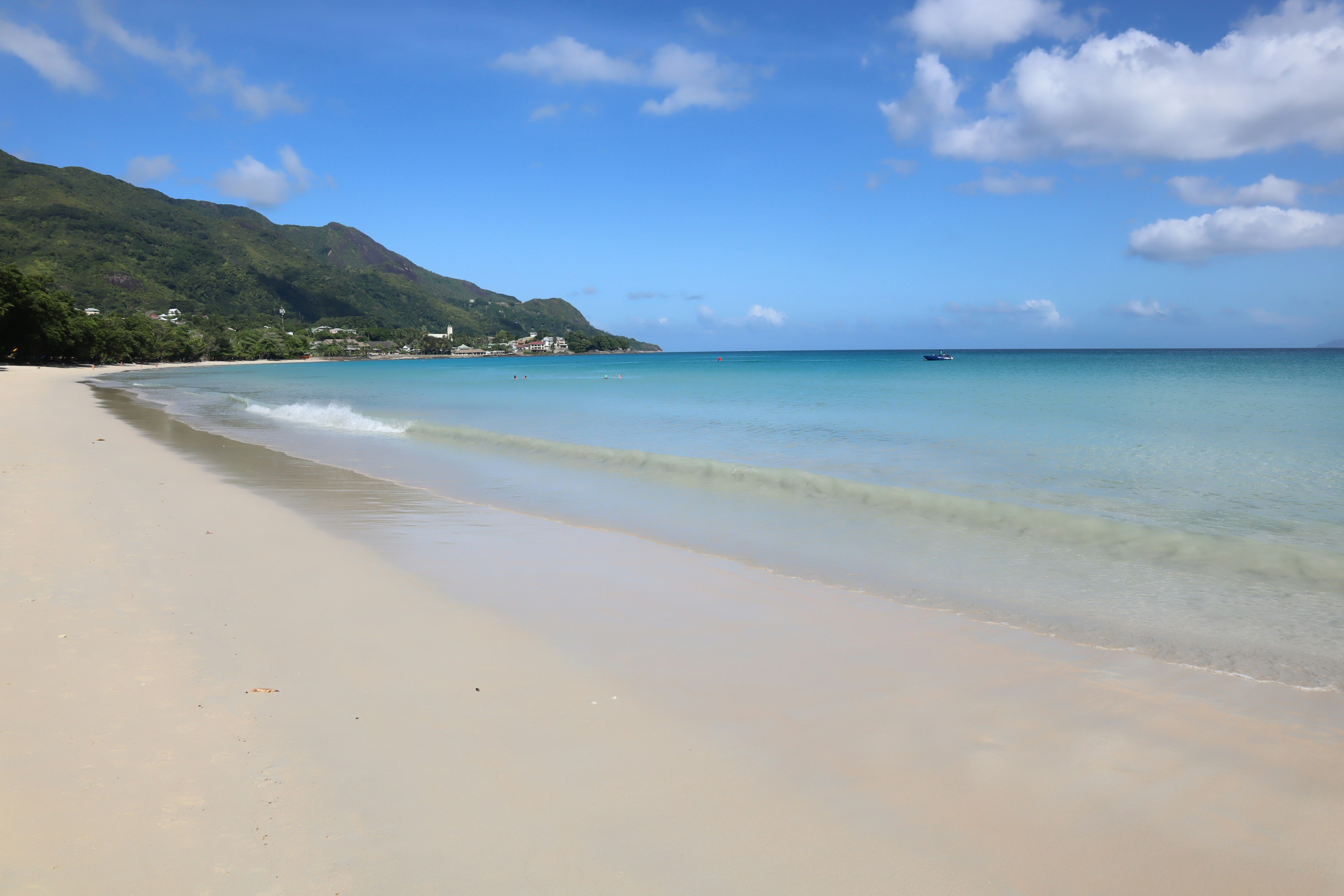 Pantai indah dengan air biru jernih dan gunung di kejauhan