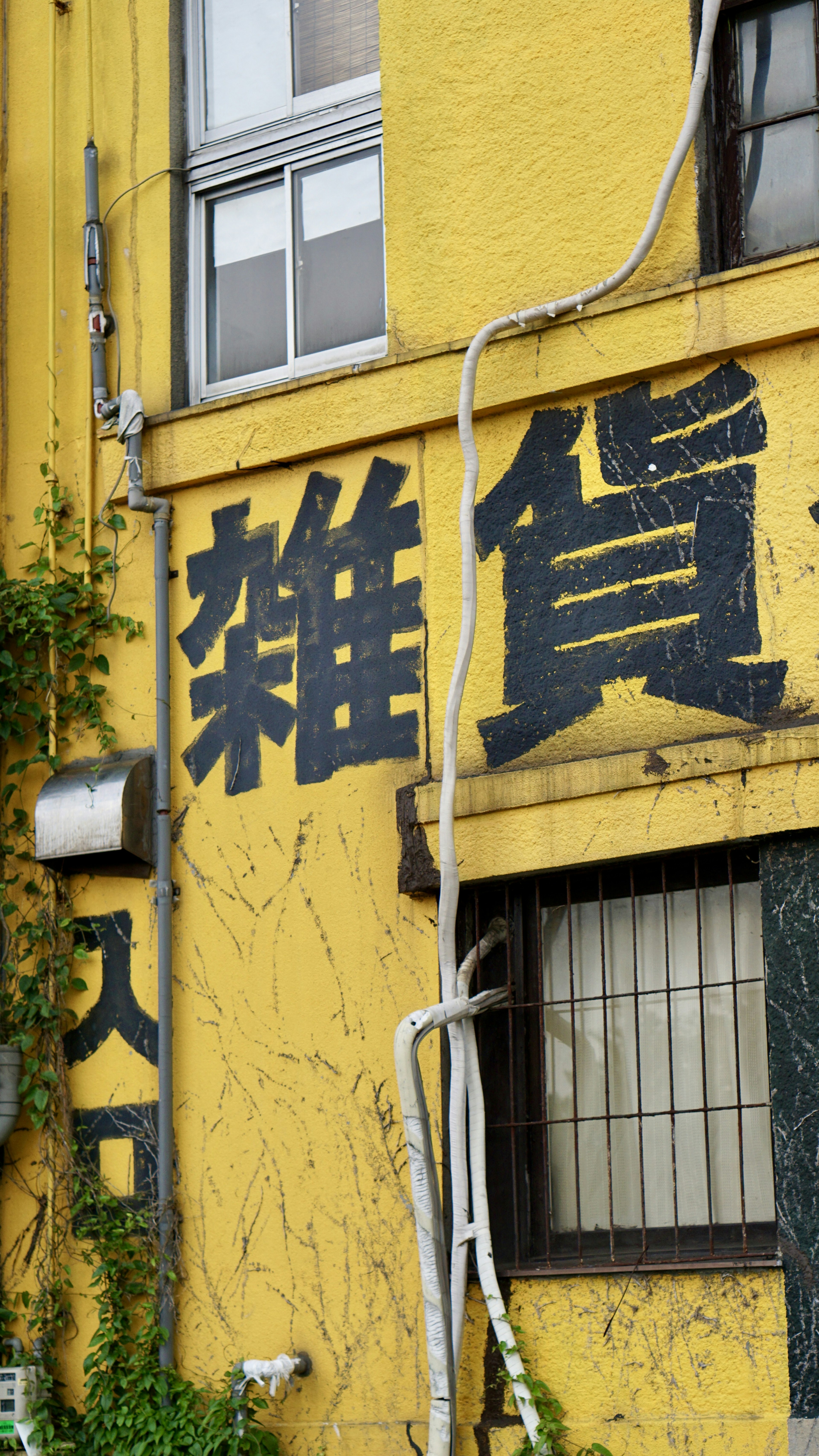 Un mur jaune avec de grands caractères noirs indiquant 'Zakka' sur un bâtiment