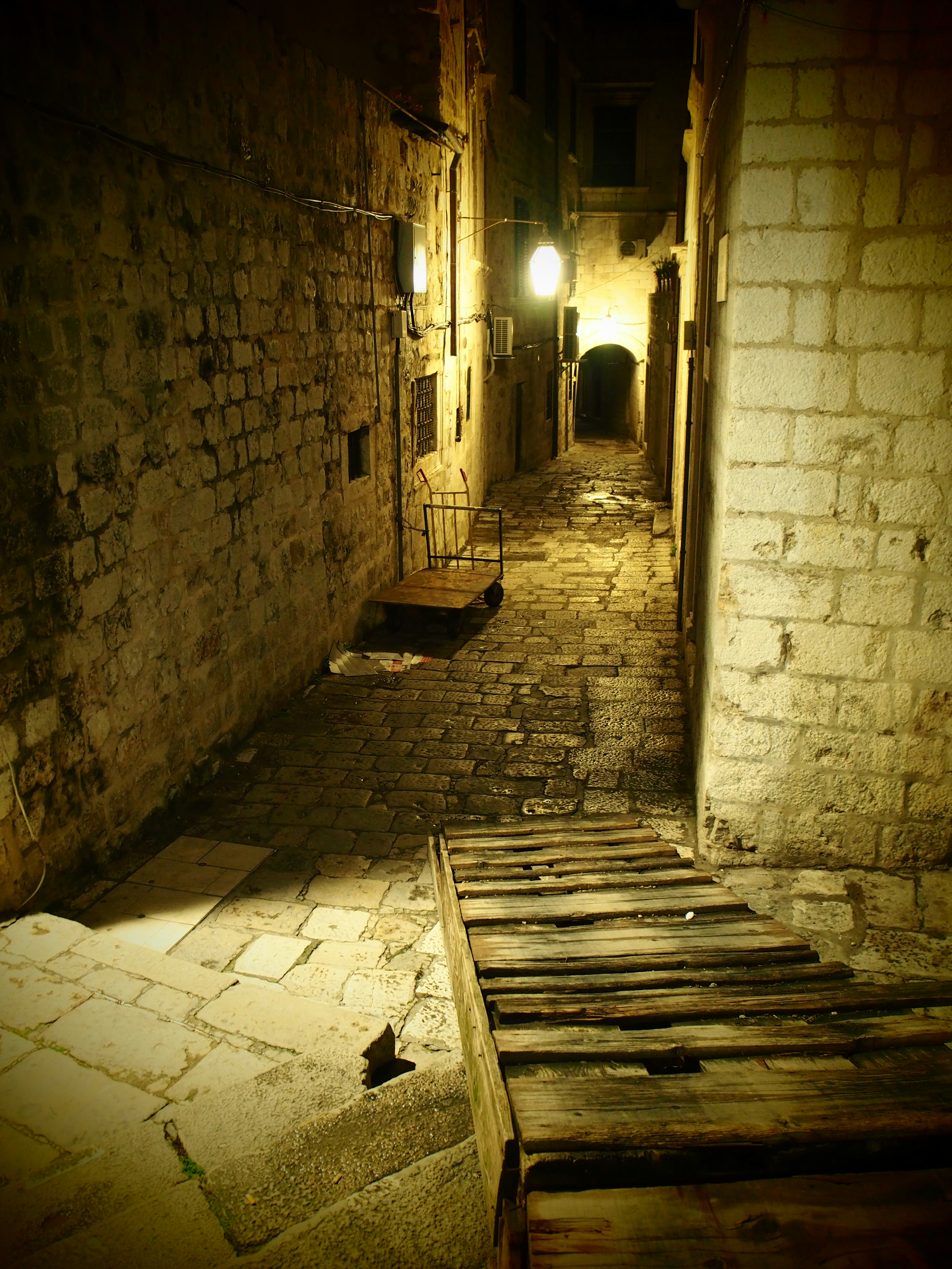 Eine schwach beleuchtete Steingasse mit einer Holztreppe bei Nacht