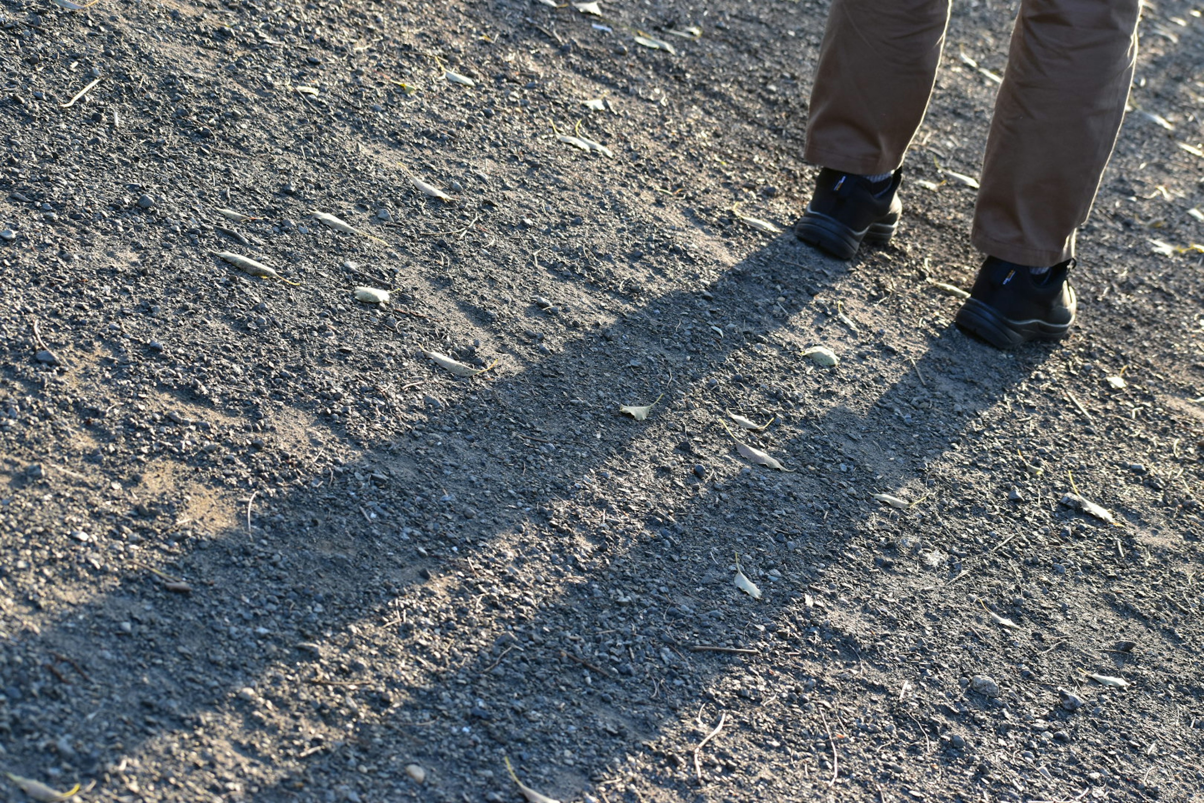 Photo of feet casting long shadows on gravel surface