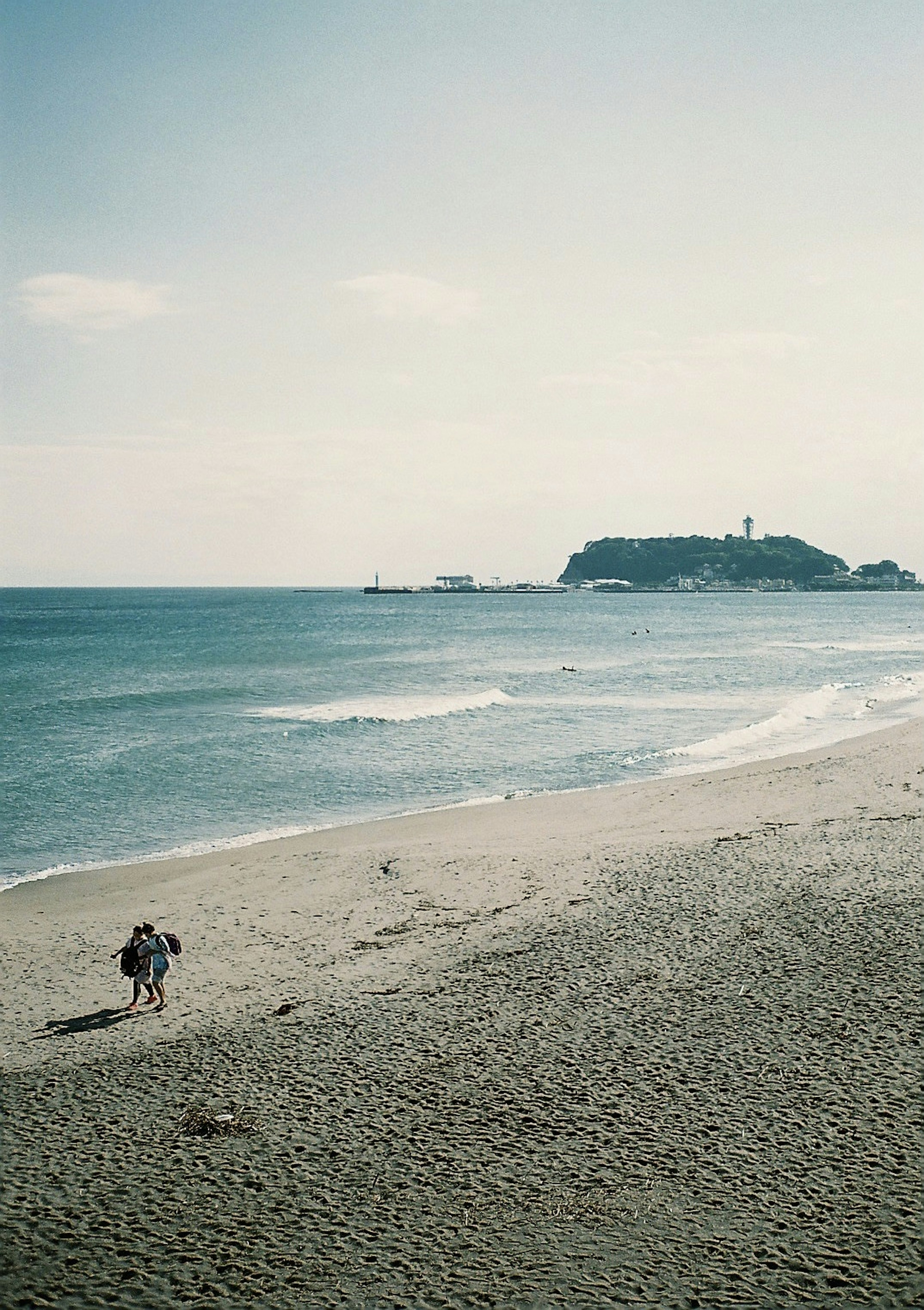 Couple walking on the beach with a calm sea and soft sky