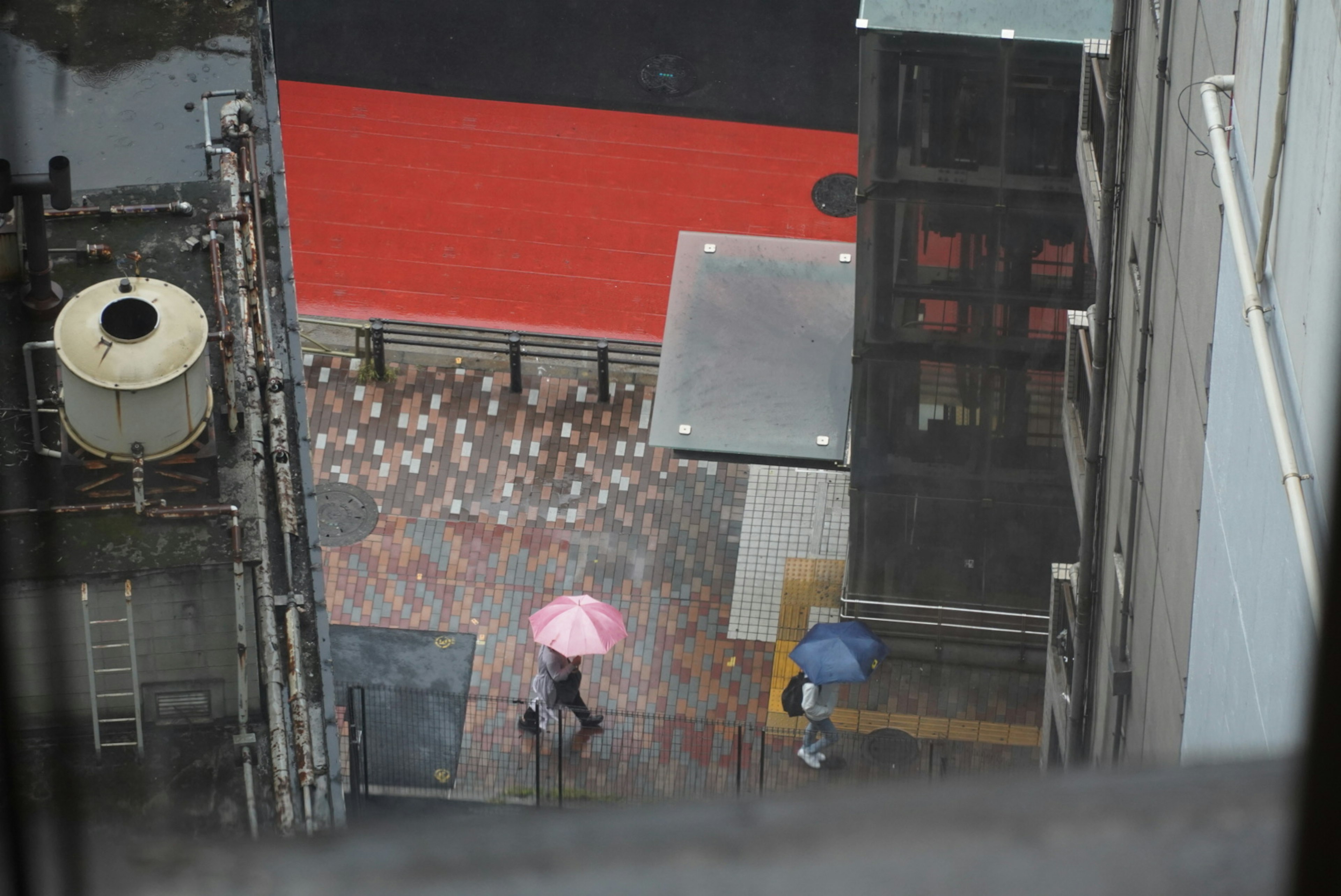 雨の中で傘をさして歩く人々 赤い床と建物の間の風景