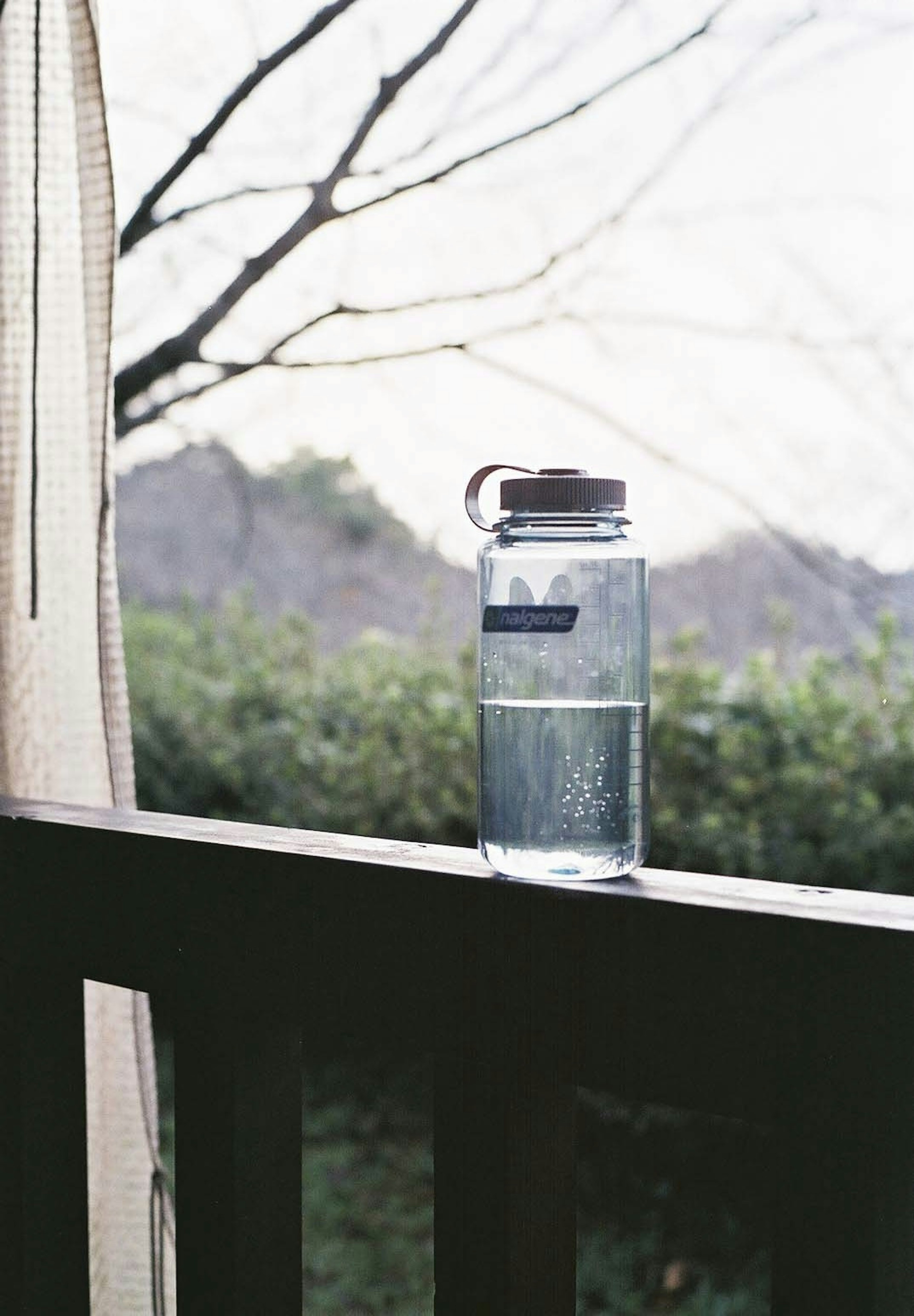 Klare Wasserflasche auf dem Balkonreling mit Bäumen im Hintergrund