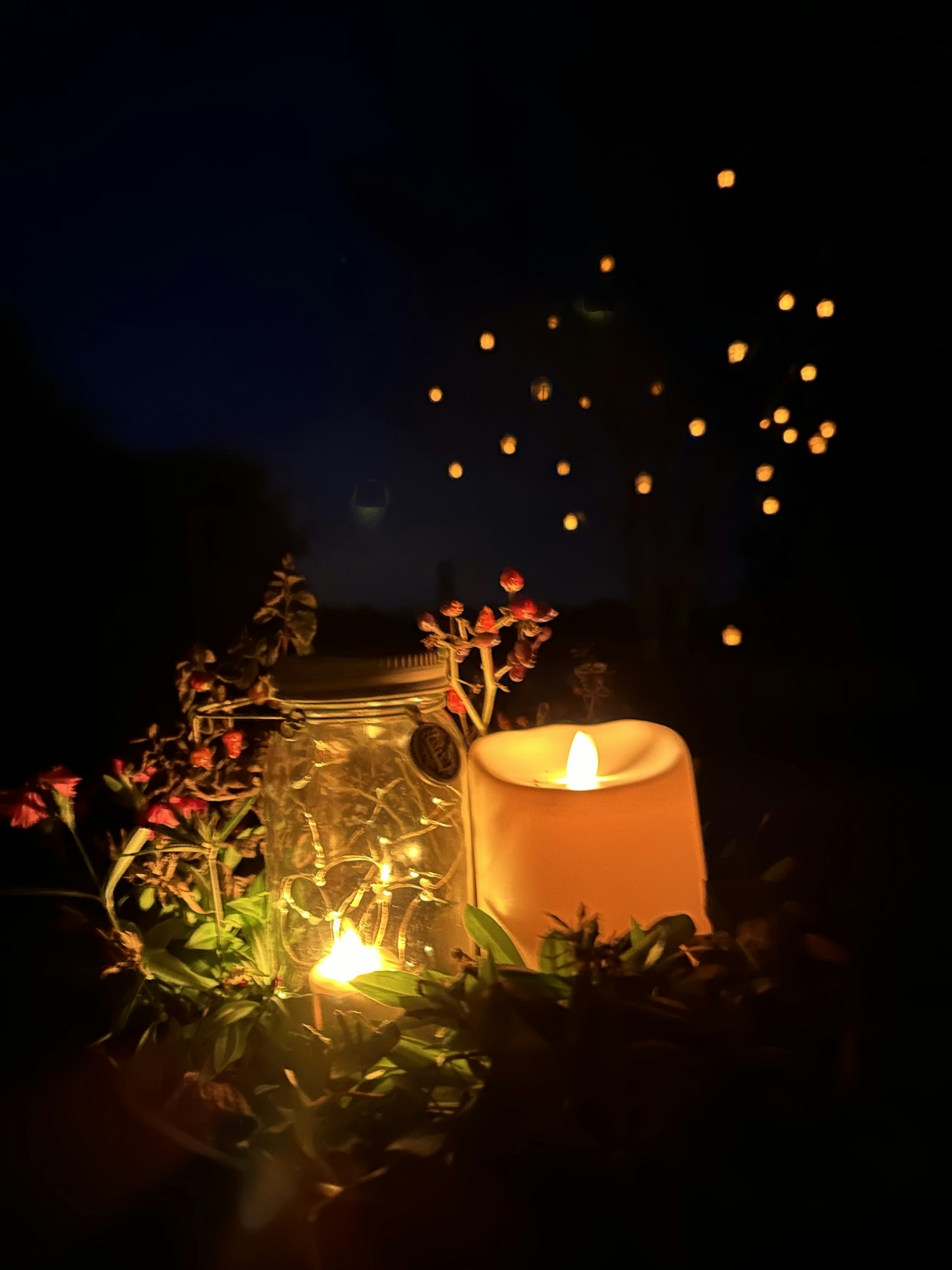 Vela rodeada de flores y frasco brillante en la noche