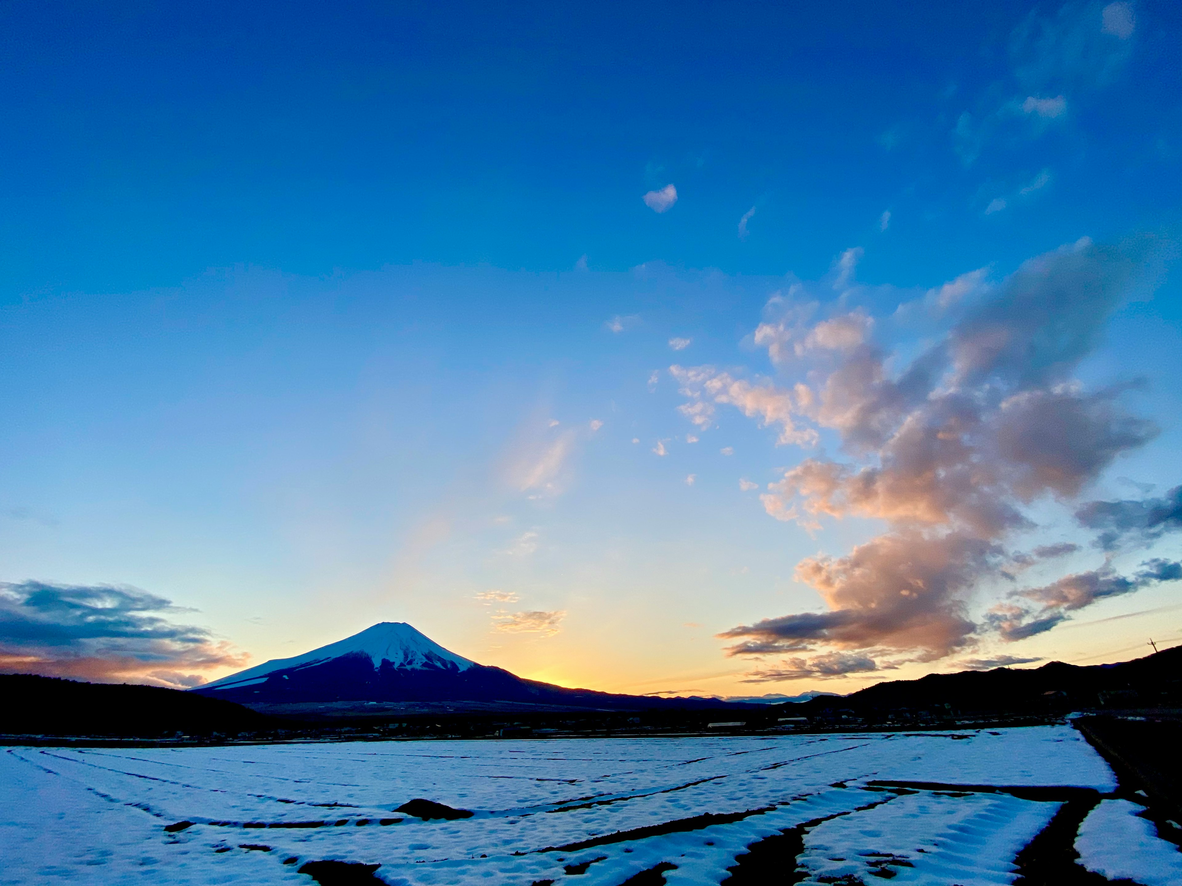 雪に覆われた田畑の向こうに富士山がそびえる美しい夕焼けの風景