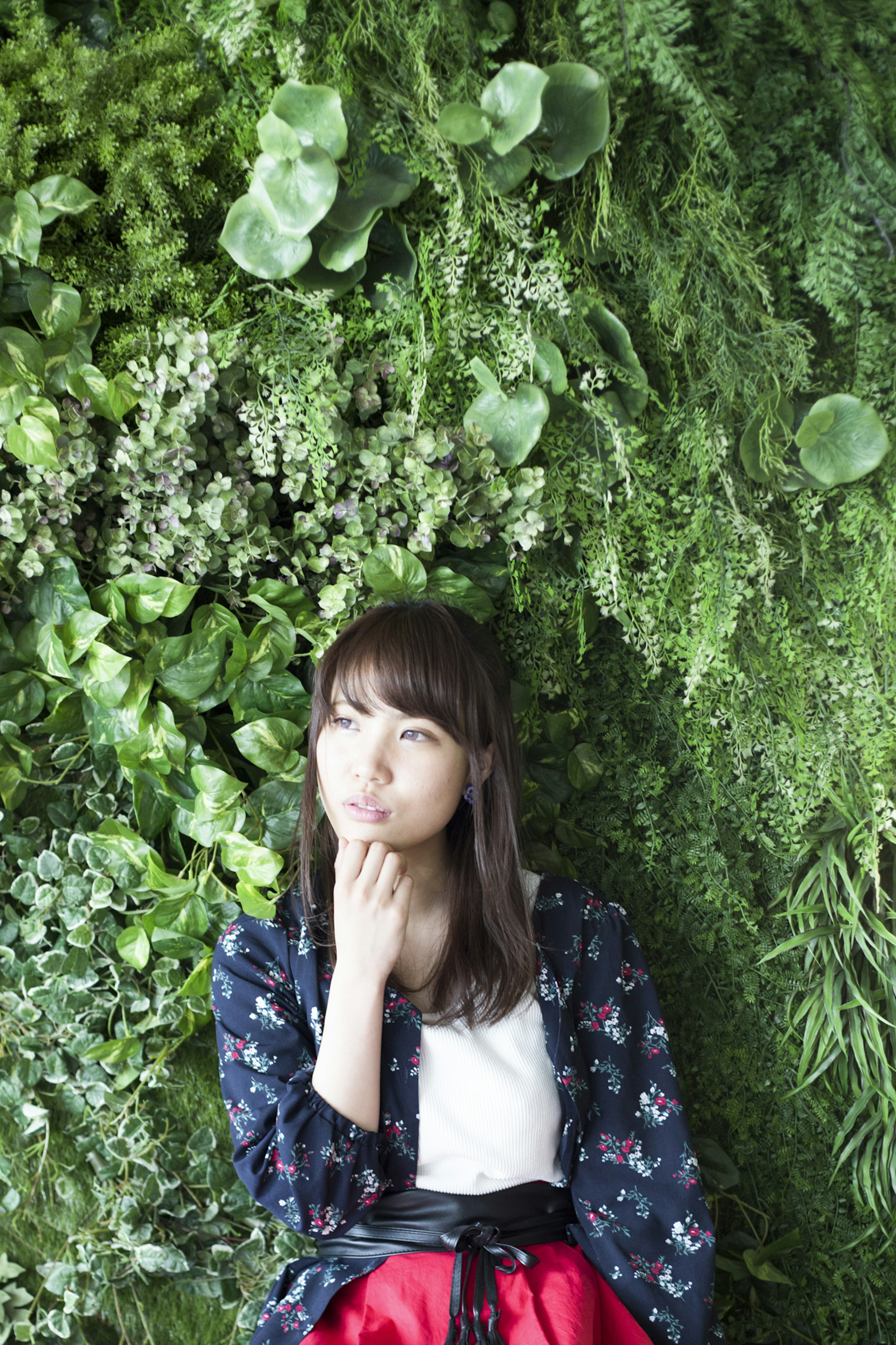 Portrait d'une femme assise devant un mur vert portant une chemise à fleurs et une jupe rouge