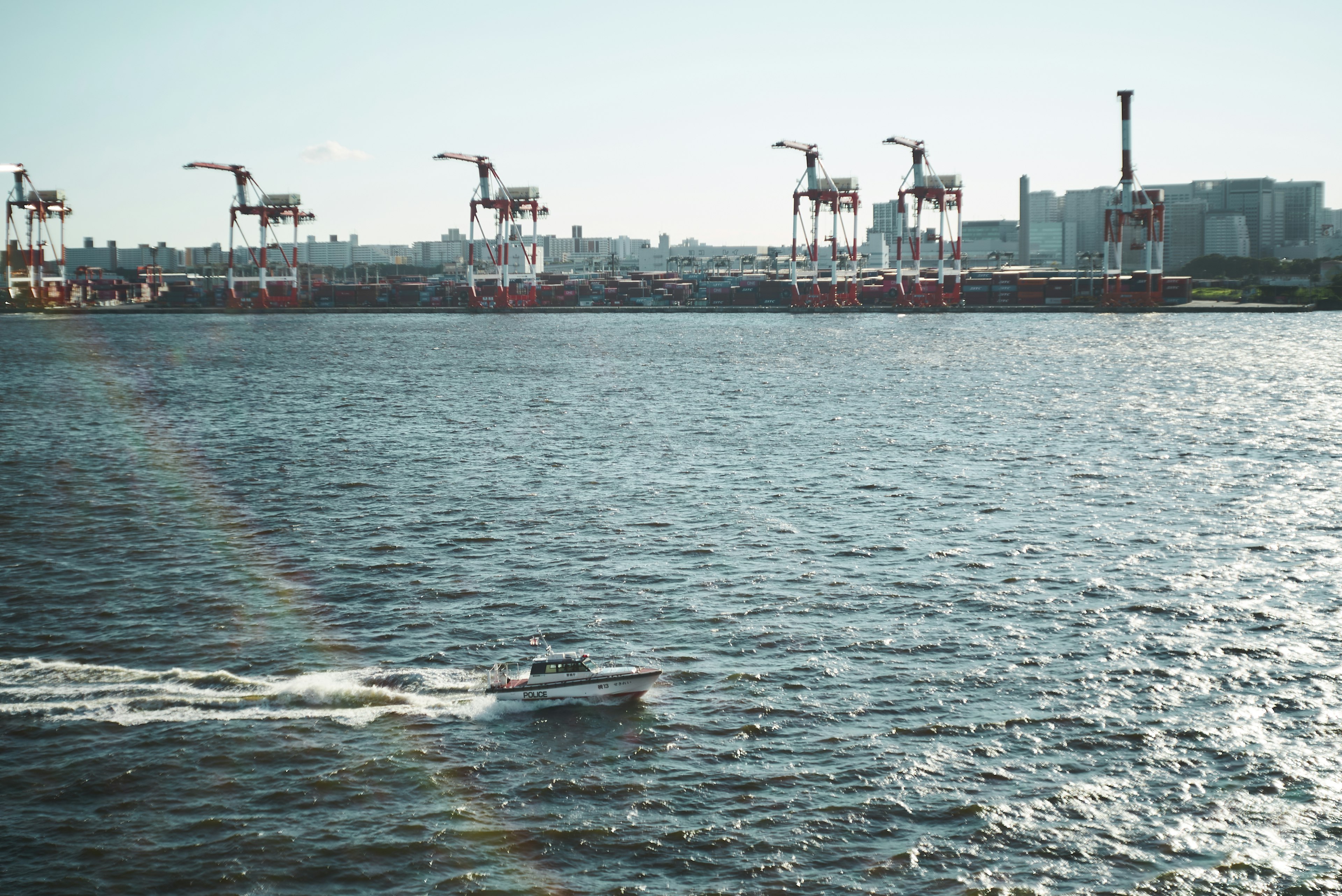 Blick auf Kräne in einem Hafen mit einem kleinen Boot, das über das Wasser fährt