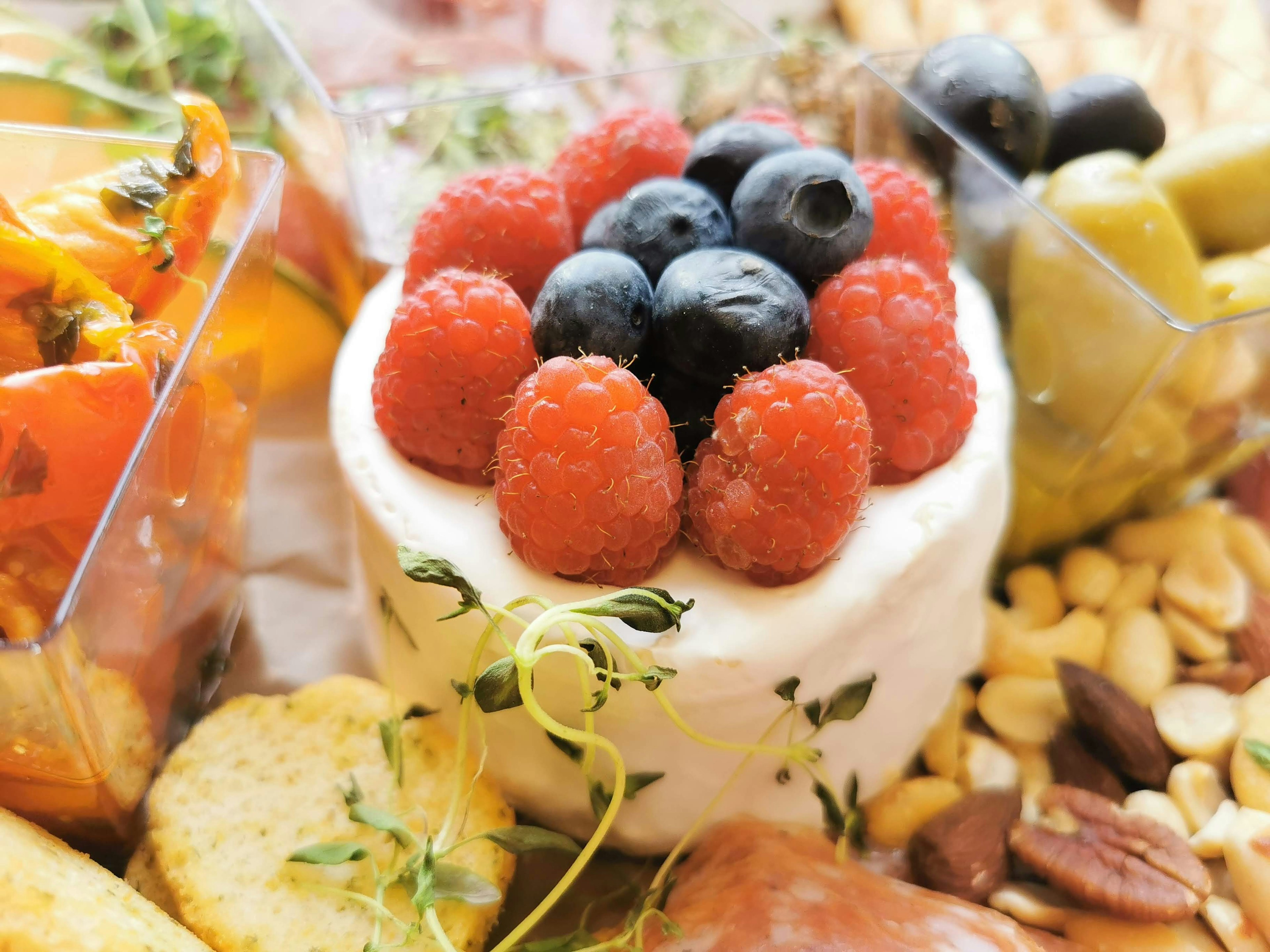 Acercamiento de un postre cubierto con frambuesas y arándanos rodeado de nueces variadas