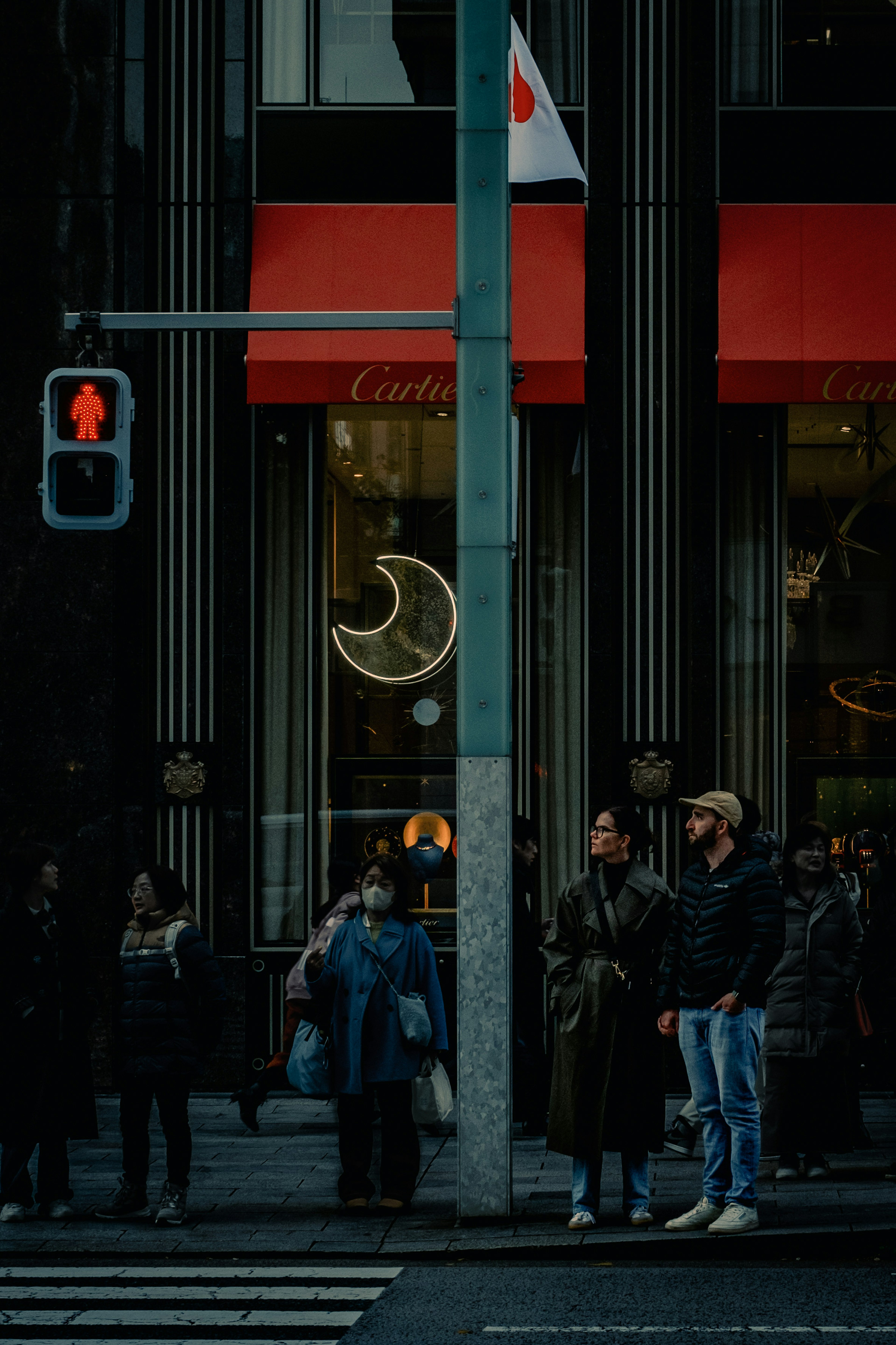 People standing at a traffic light in front of a store with a red sign