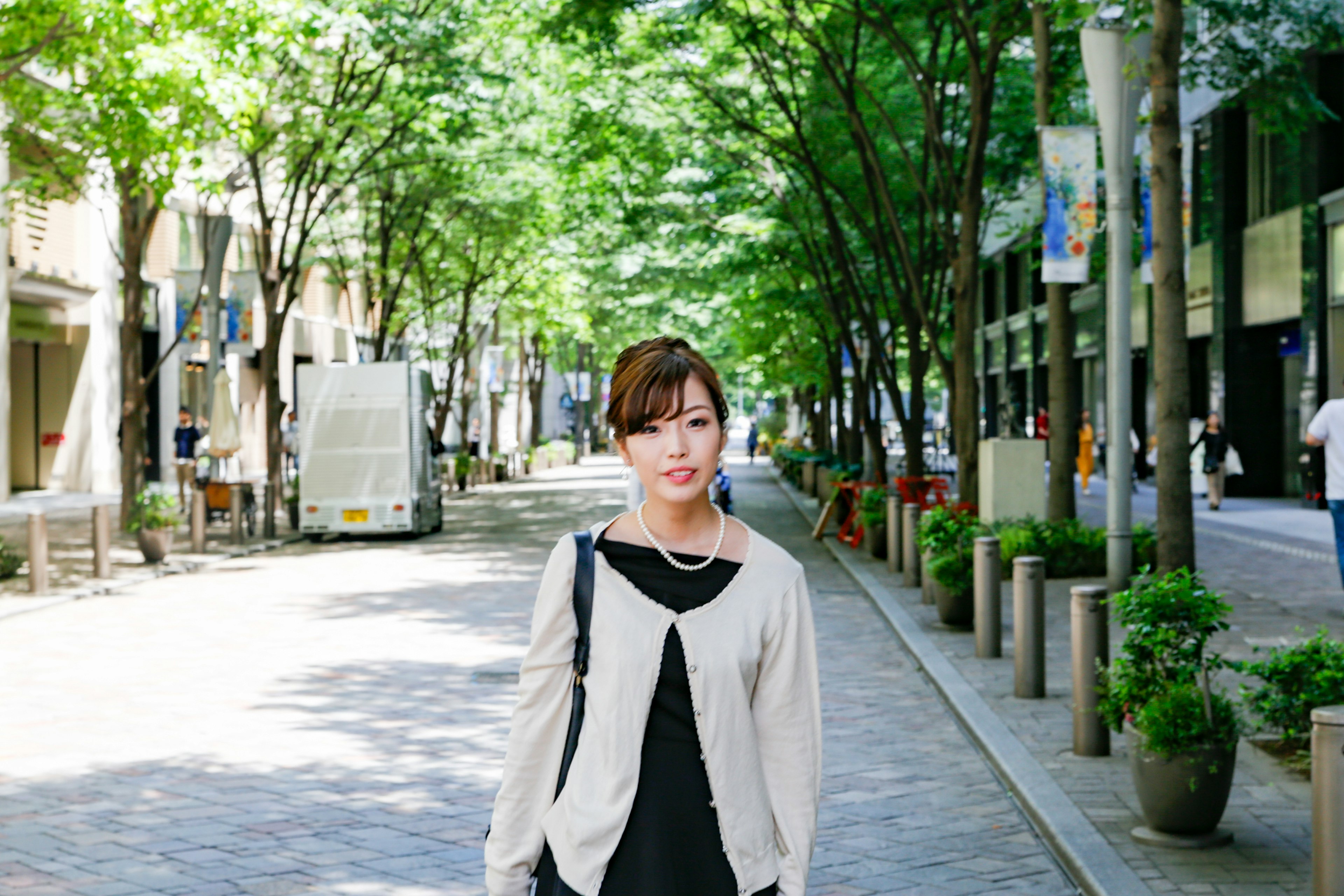 A woman standing on an urban street surrounded by green trees