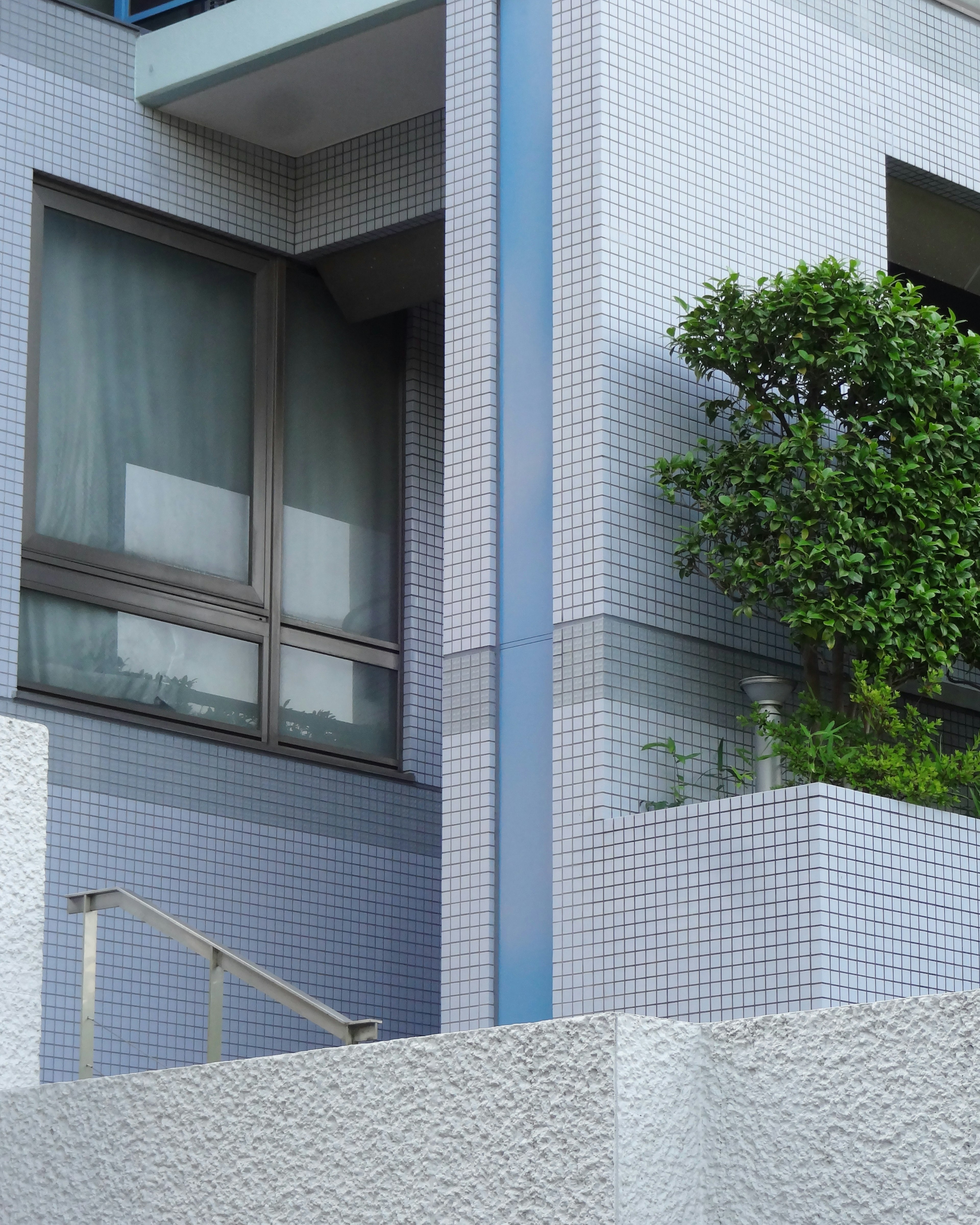 Part of a building with blue tiled exterior and green plants