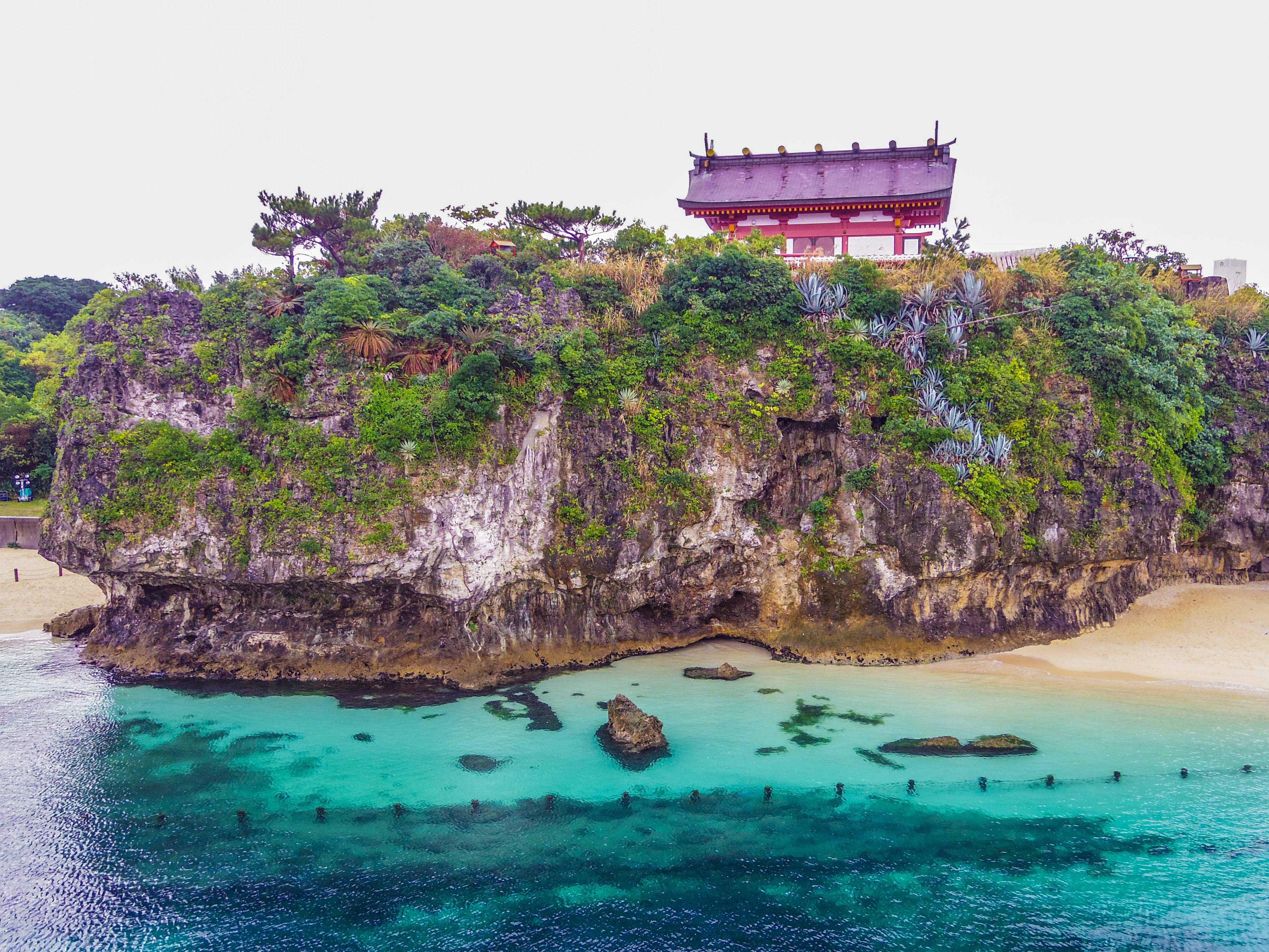 岩石上有红色屋顶的建筑，周围环绕着清澈的蓝色海水和绿色植被