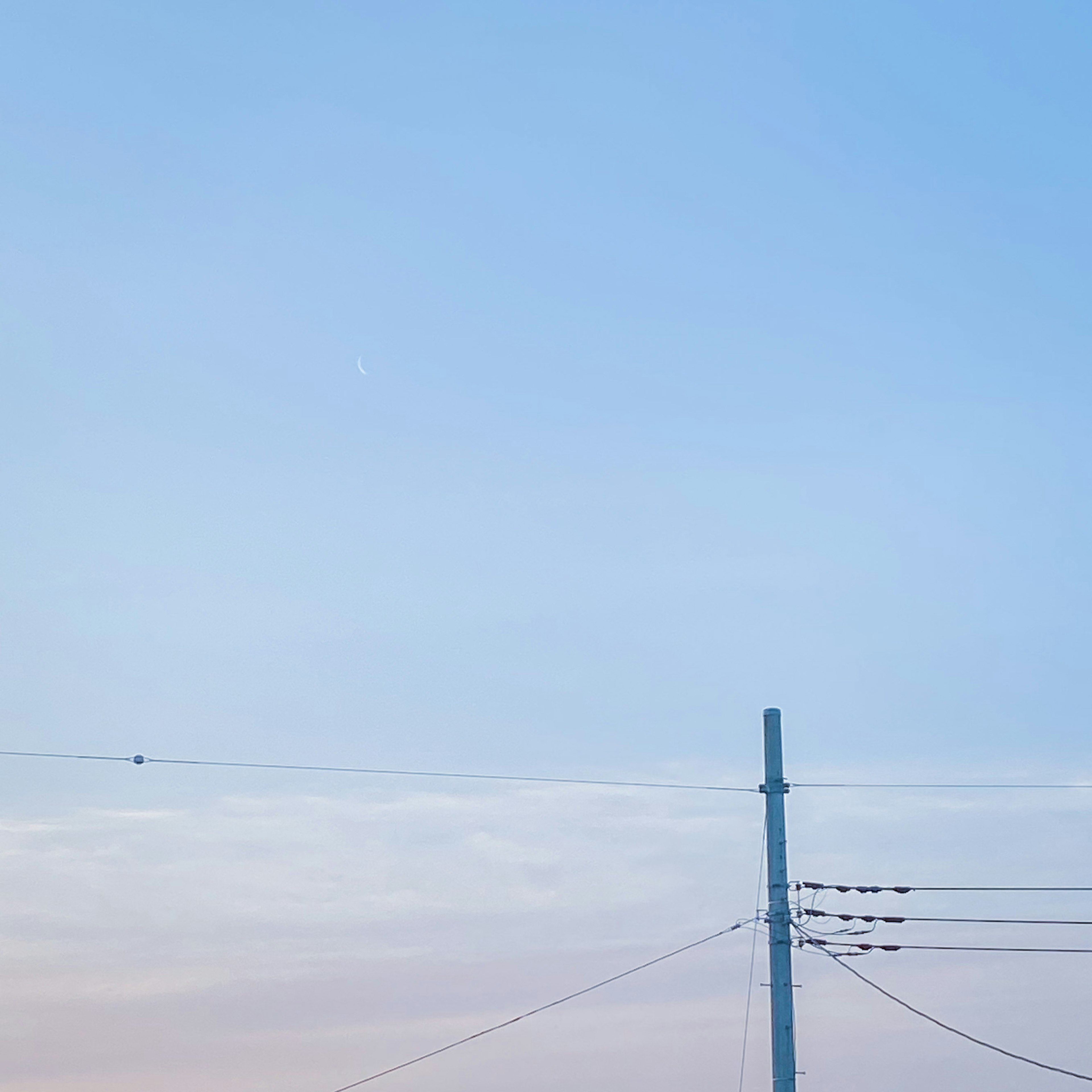 A utility pole and power lines against a blue sky with soft clouds