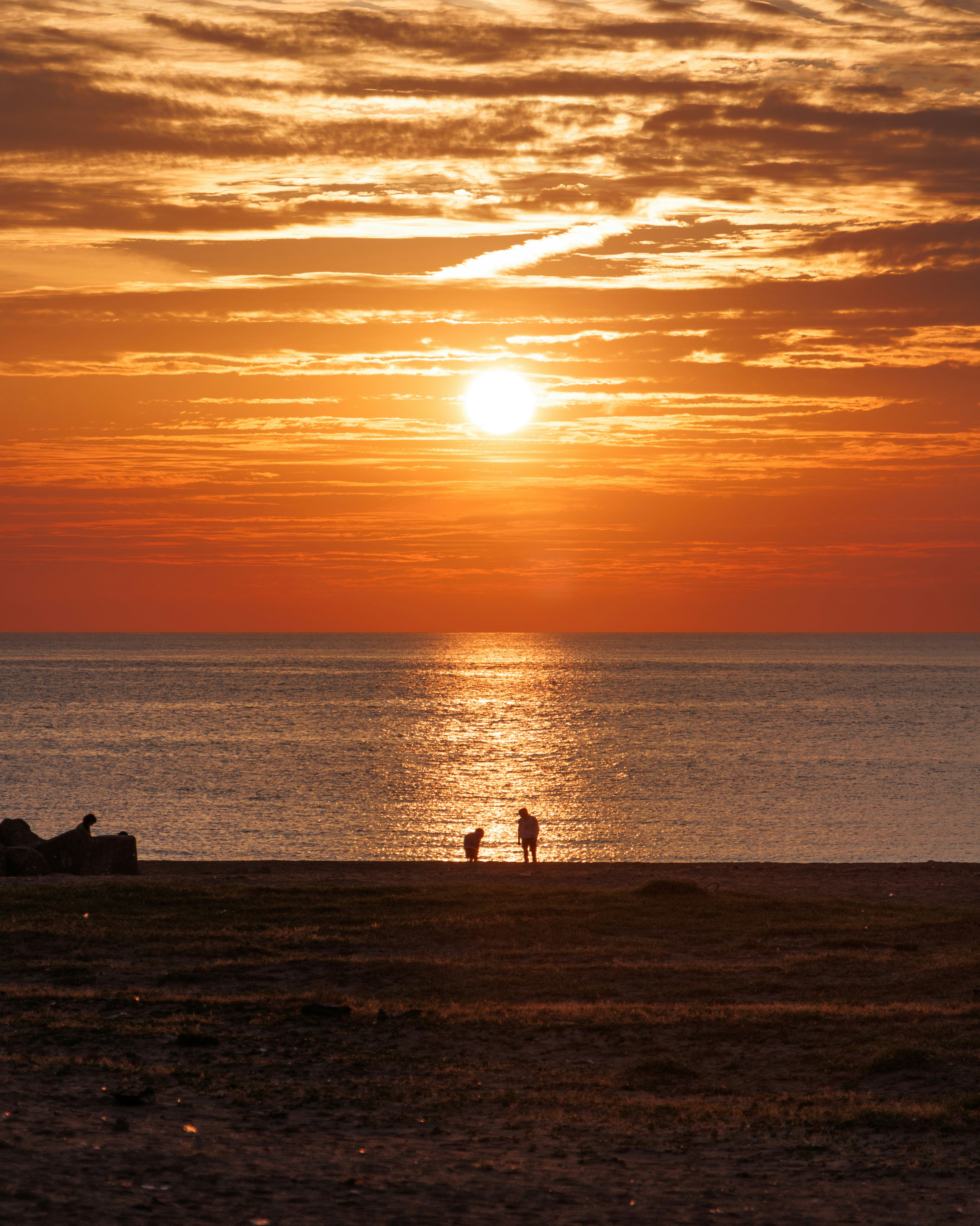 Silueta de personas caminando en la playa al atardecer con tonos naranjas vibrantes