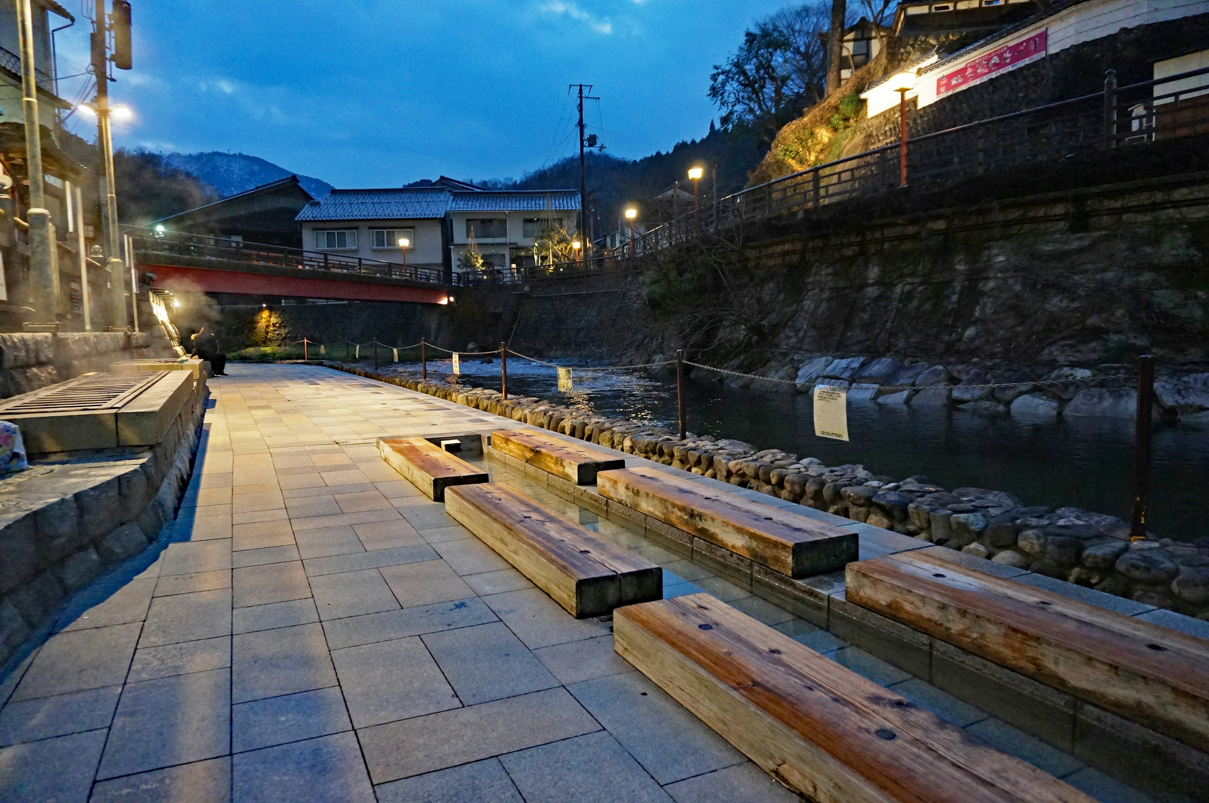 Wooden benches along a riverside walkway in a nighttime hot spring town