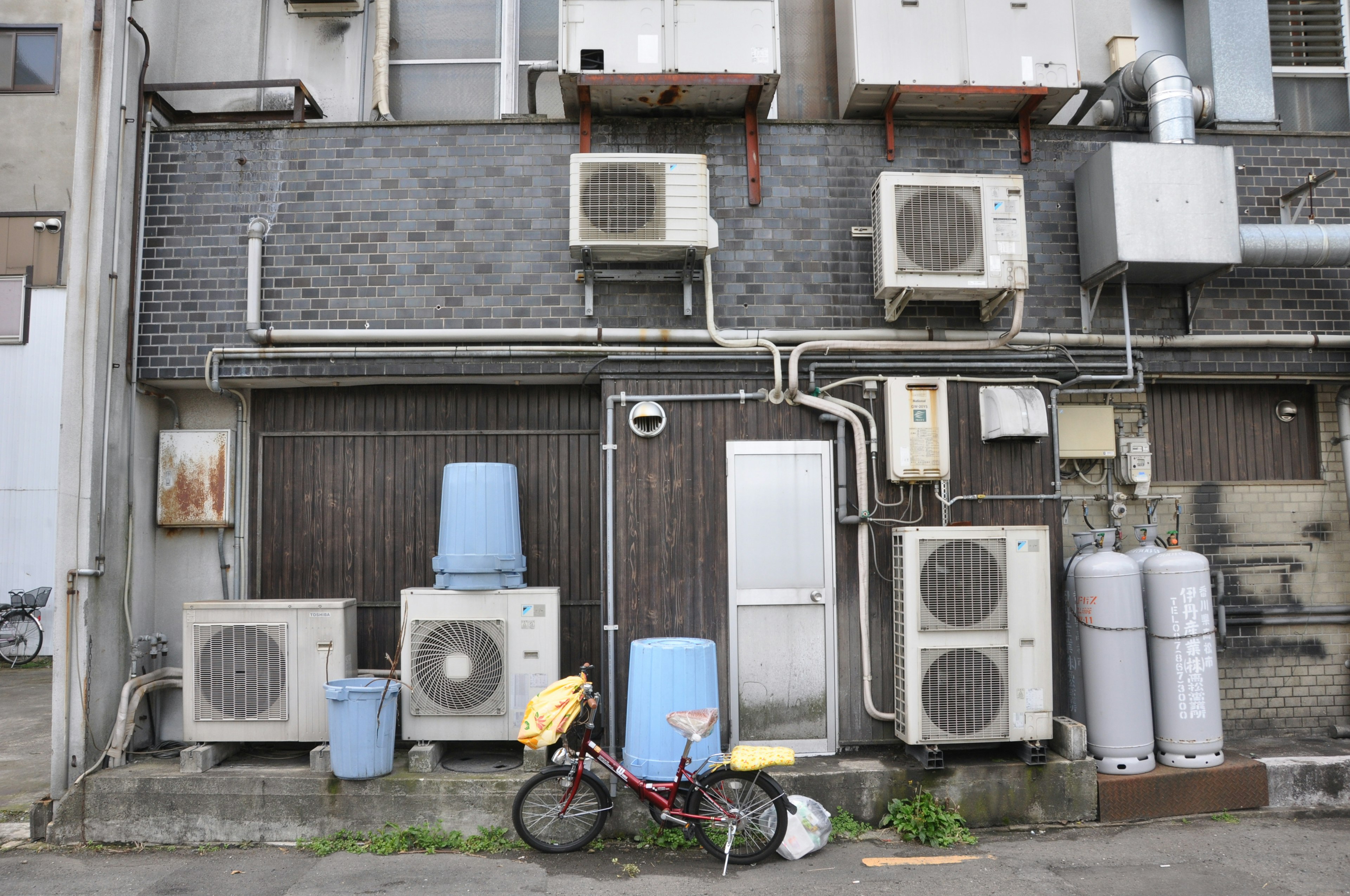 Rear view of a building with air conditioning units blue buckets and a bicycle