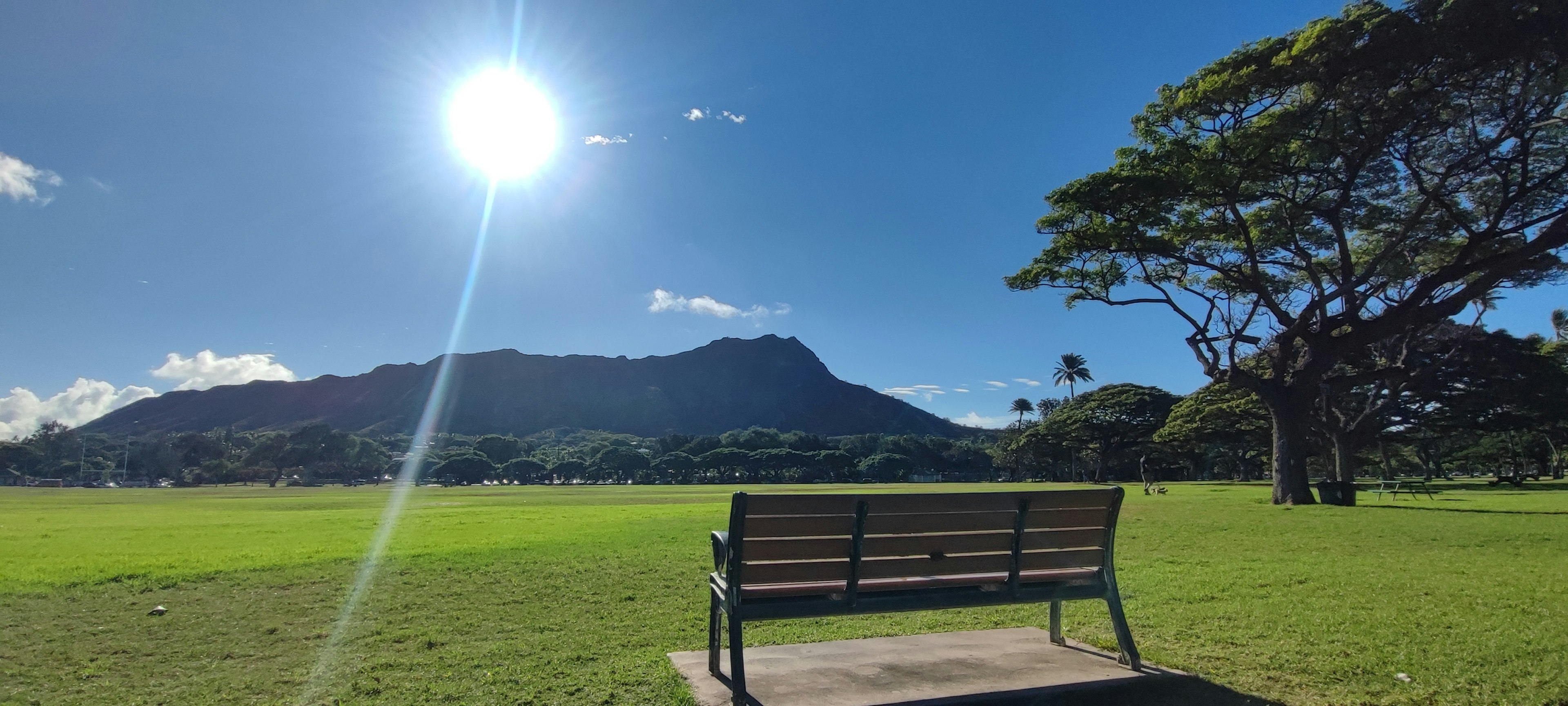 青空と太陽の下にあるベンチと山の風景