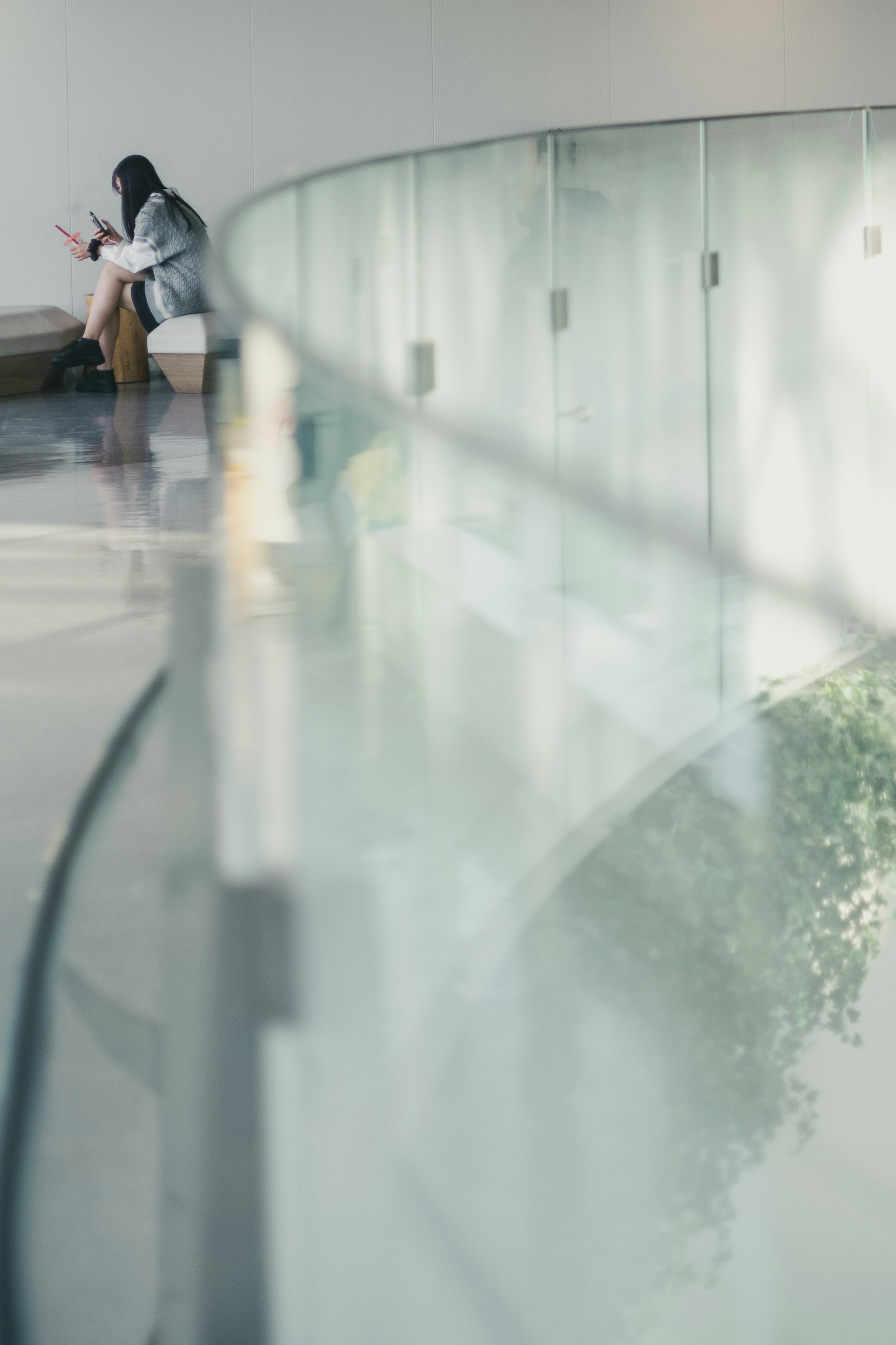 Une femme assise tranquillement dans un espace intérieur moderne avec une rampe en verre transparent et de la verdure visible