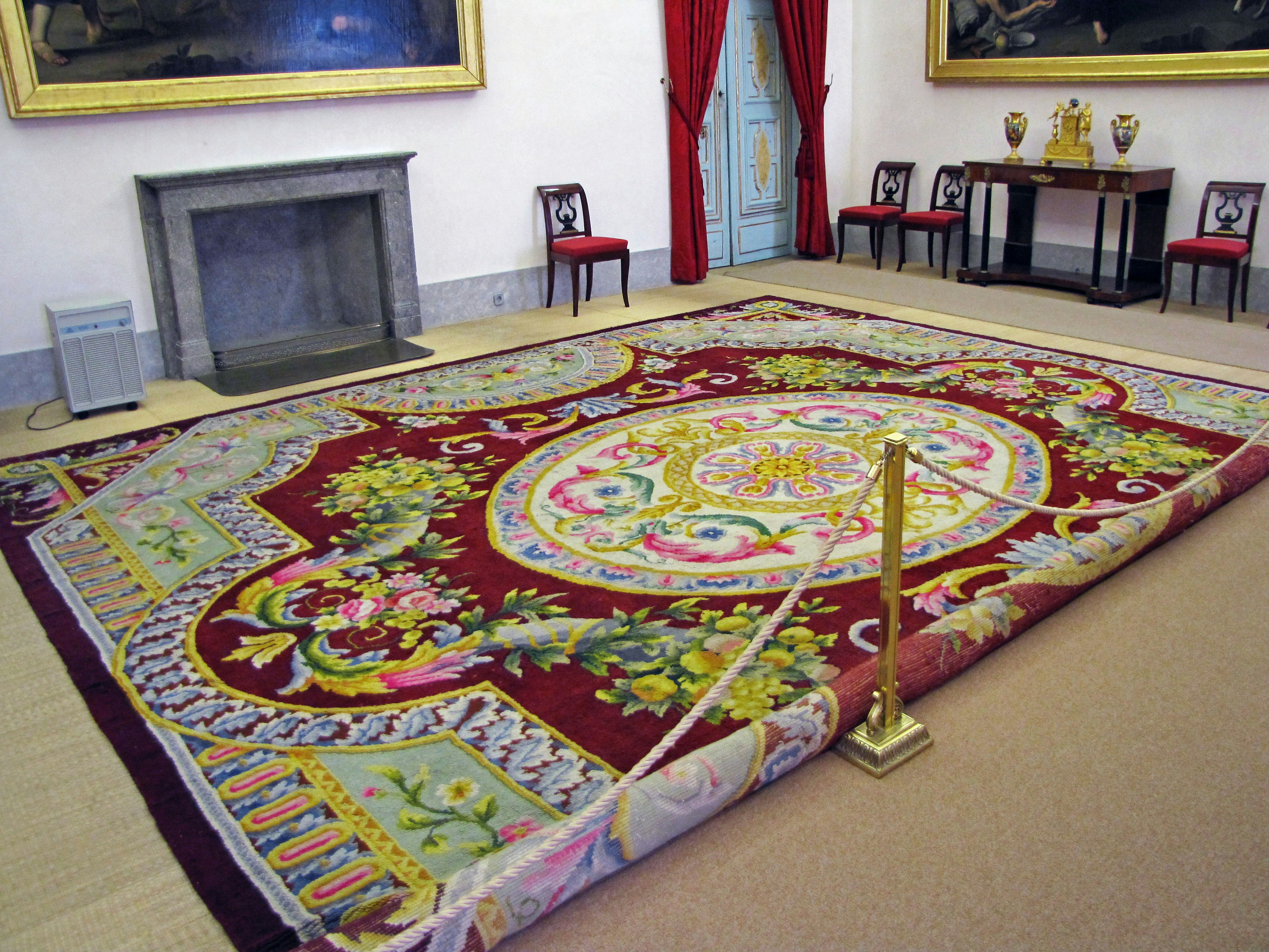 Interior of a room featuring a luxurious patterned rug red curtains and paintings in the background