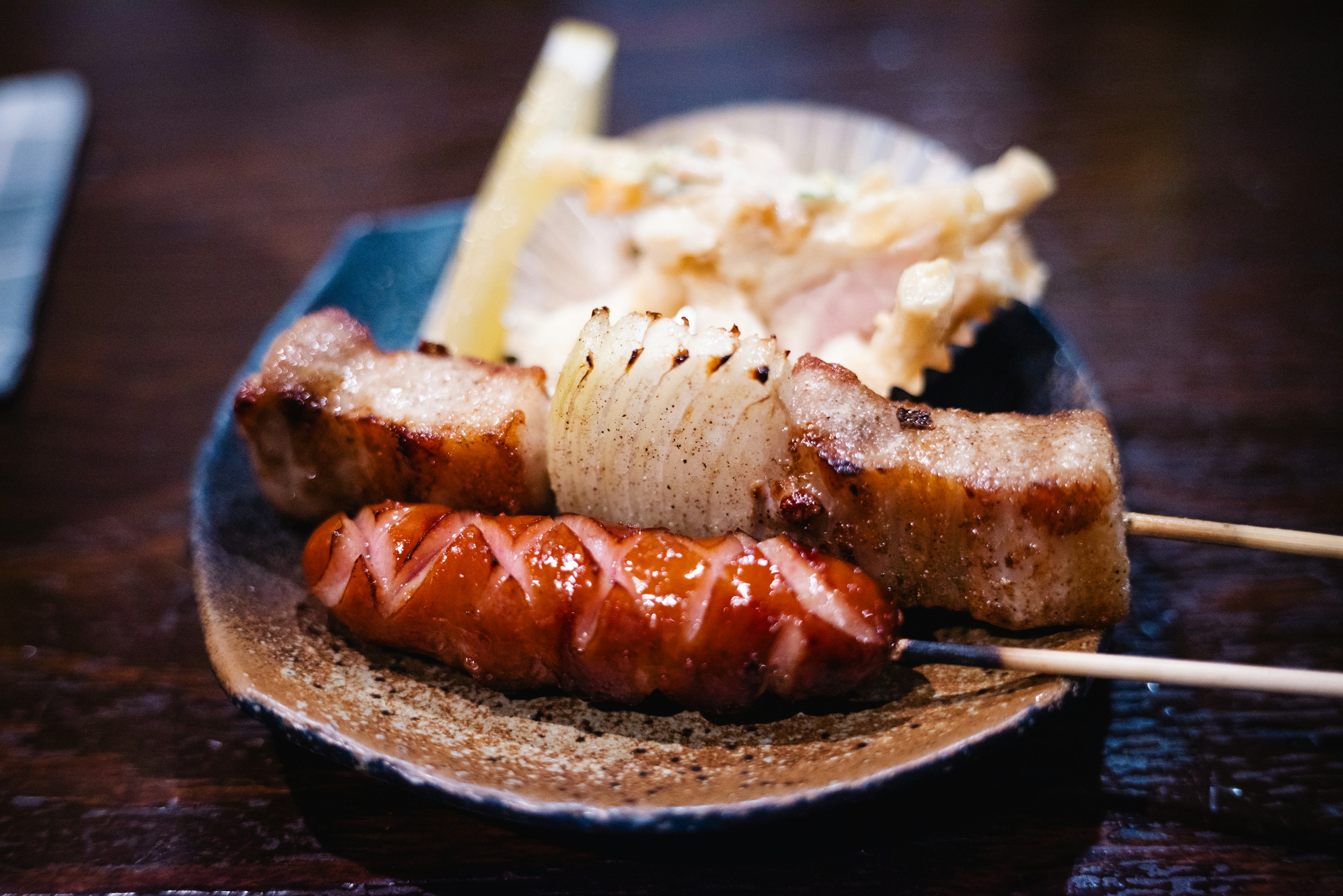 A plate featuring grilled pork belly and sausage with garnishes