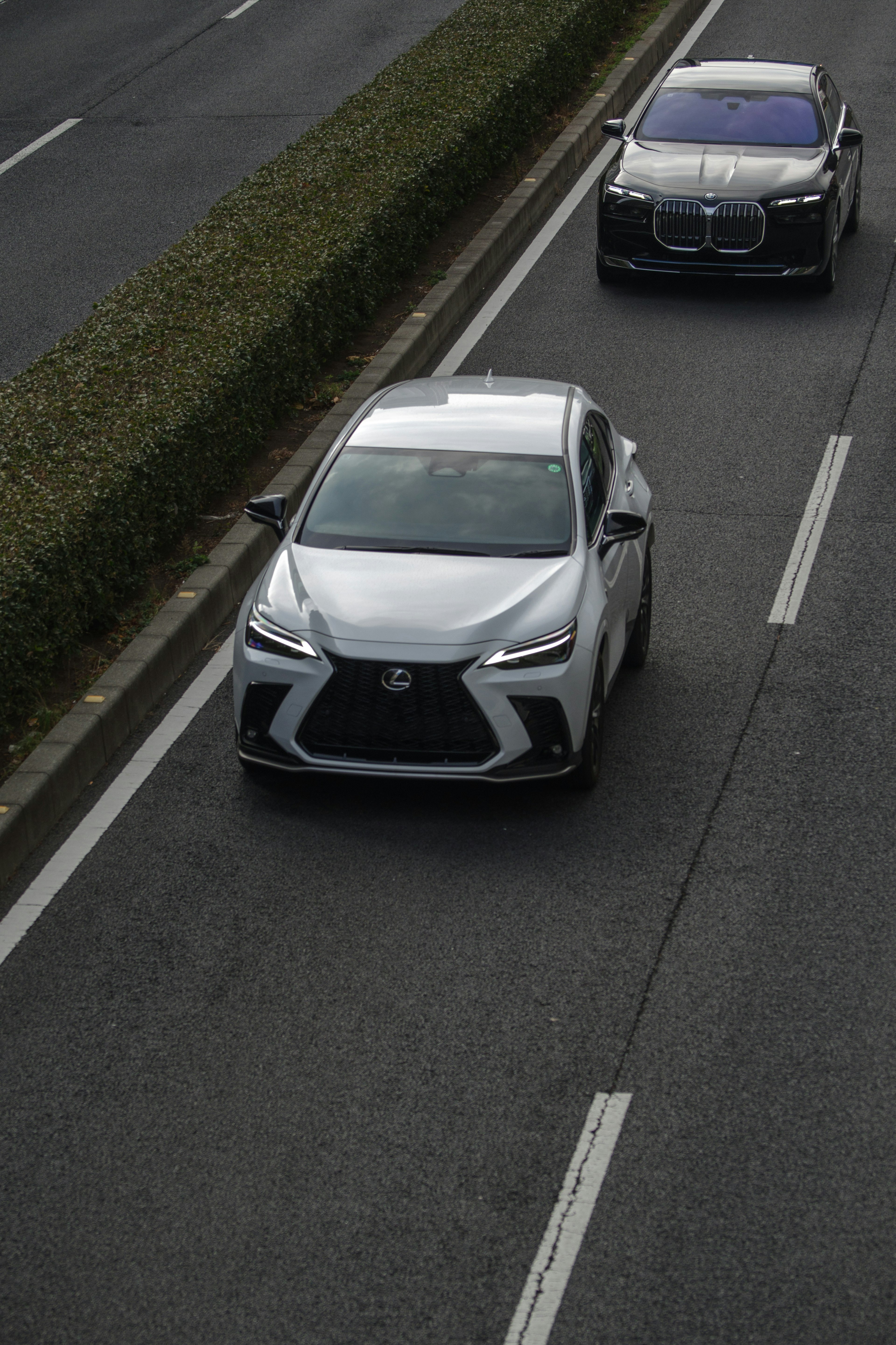 A silver Lexus car driving on a road with a black car behind it