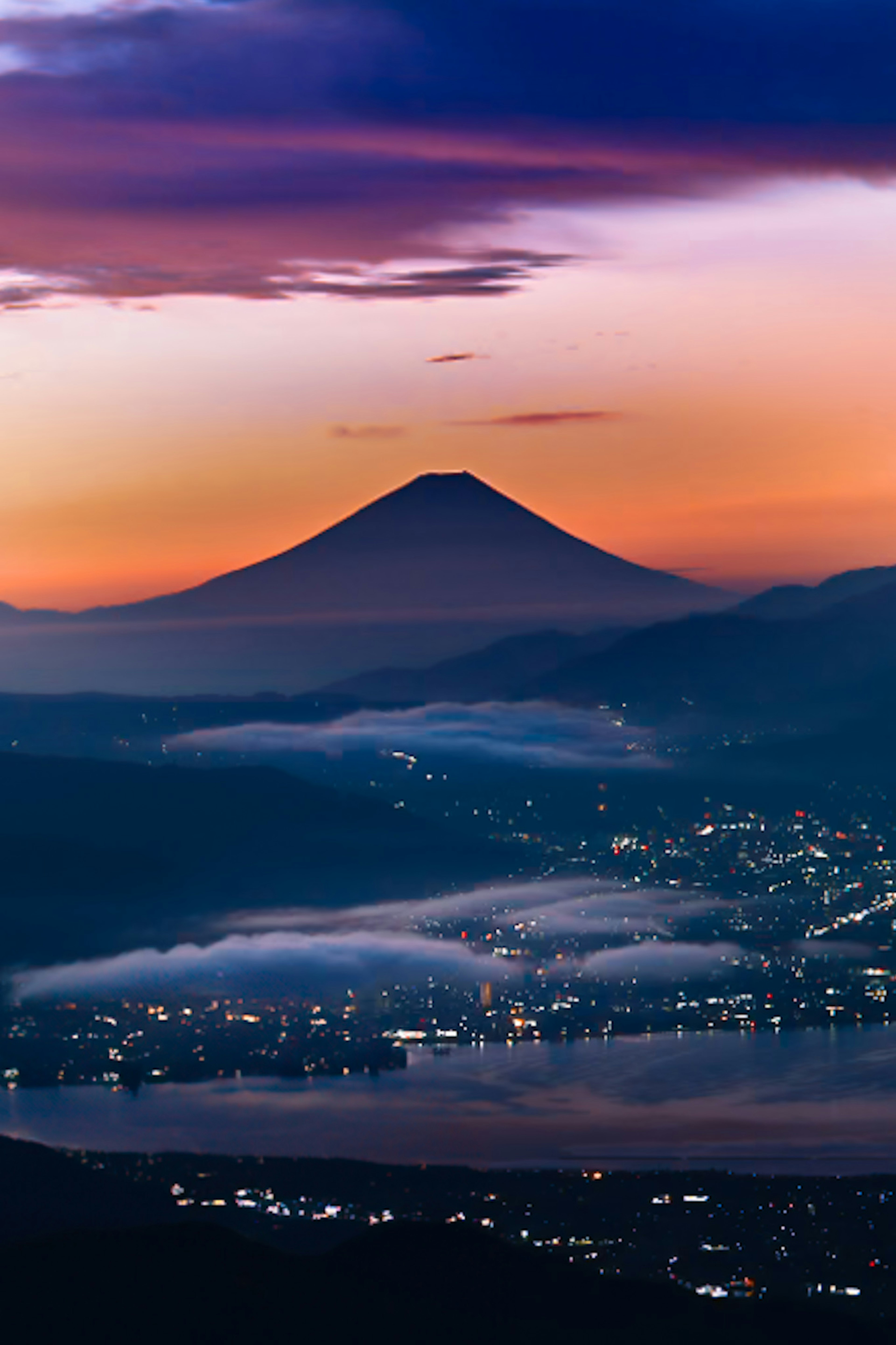 Gunung Fuji dengan latar belakang matahari terbenam yang berwarna-warni dan lembah berkabut di bawahnya