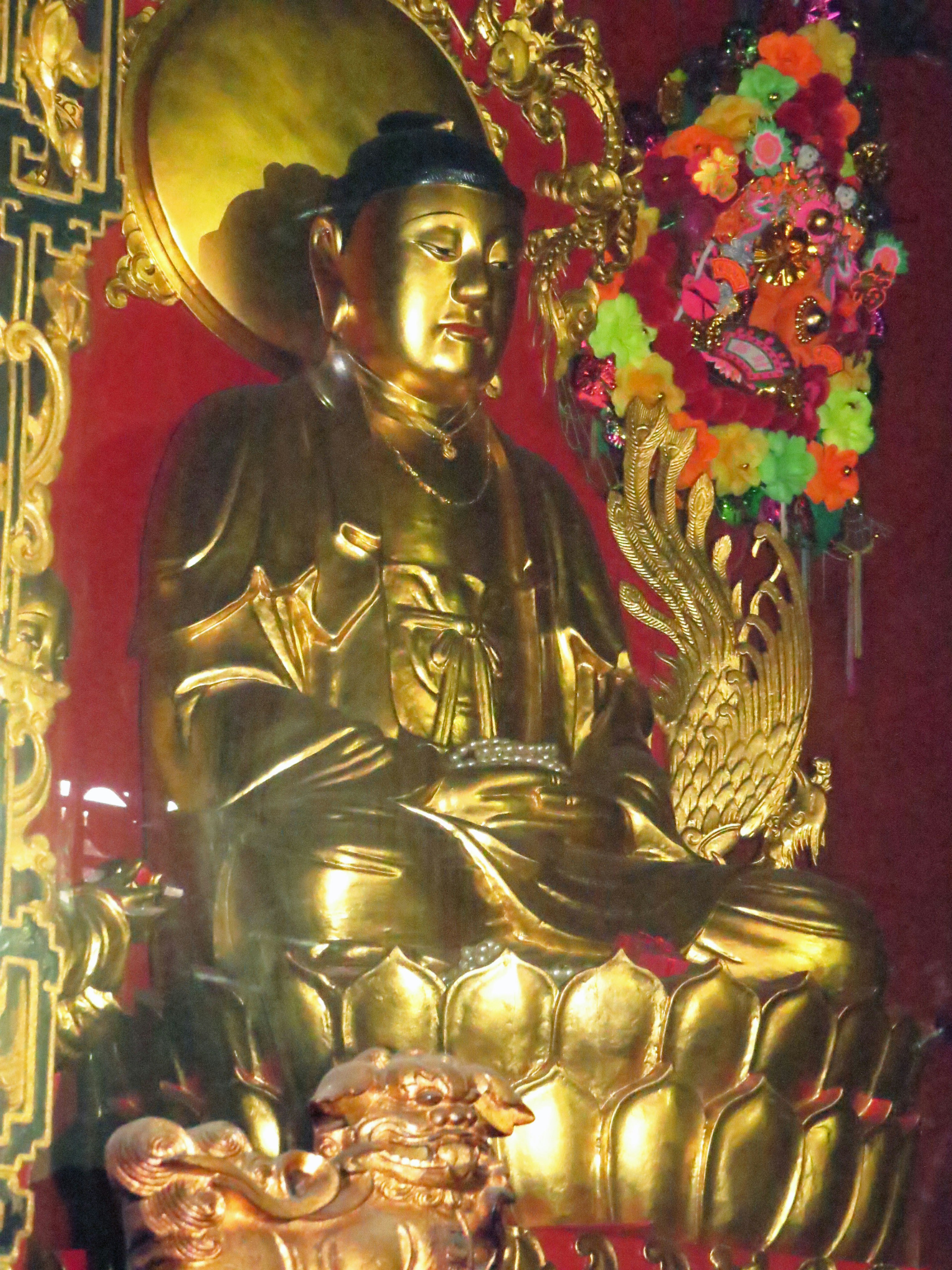 Goldene Statue eines sitzenden Buddha mit bunten Blumenarrangements im Hintergrund