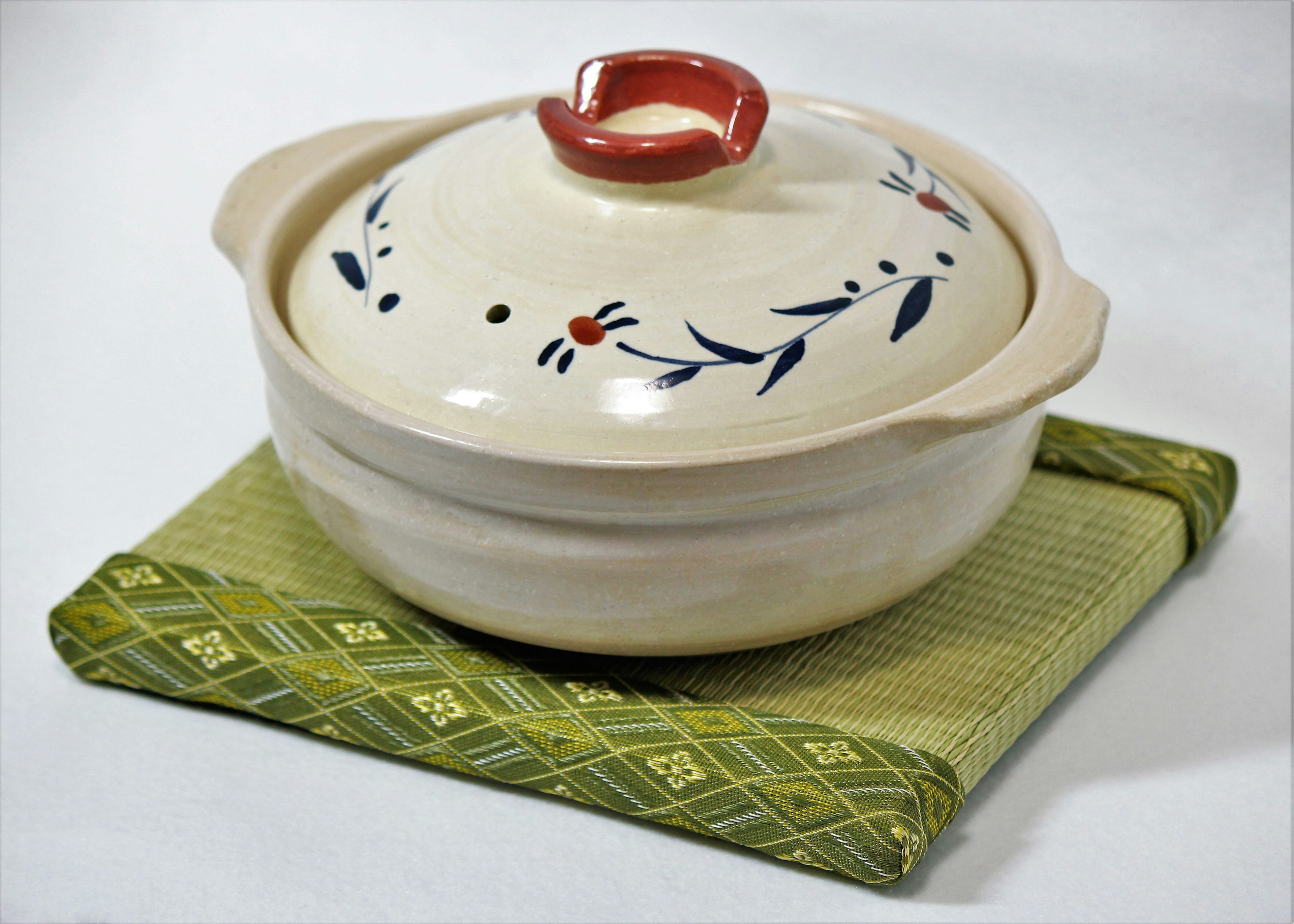 Beautifully designed ceramic pot with a red lid placed on a green mat