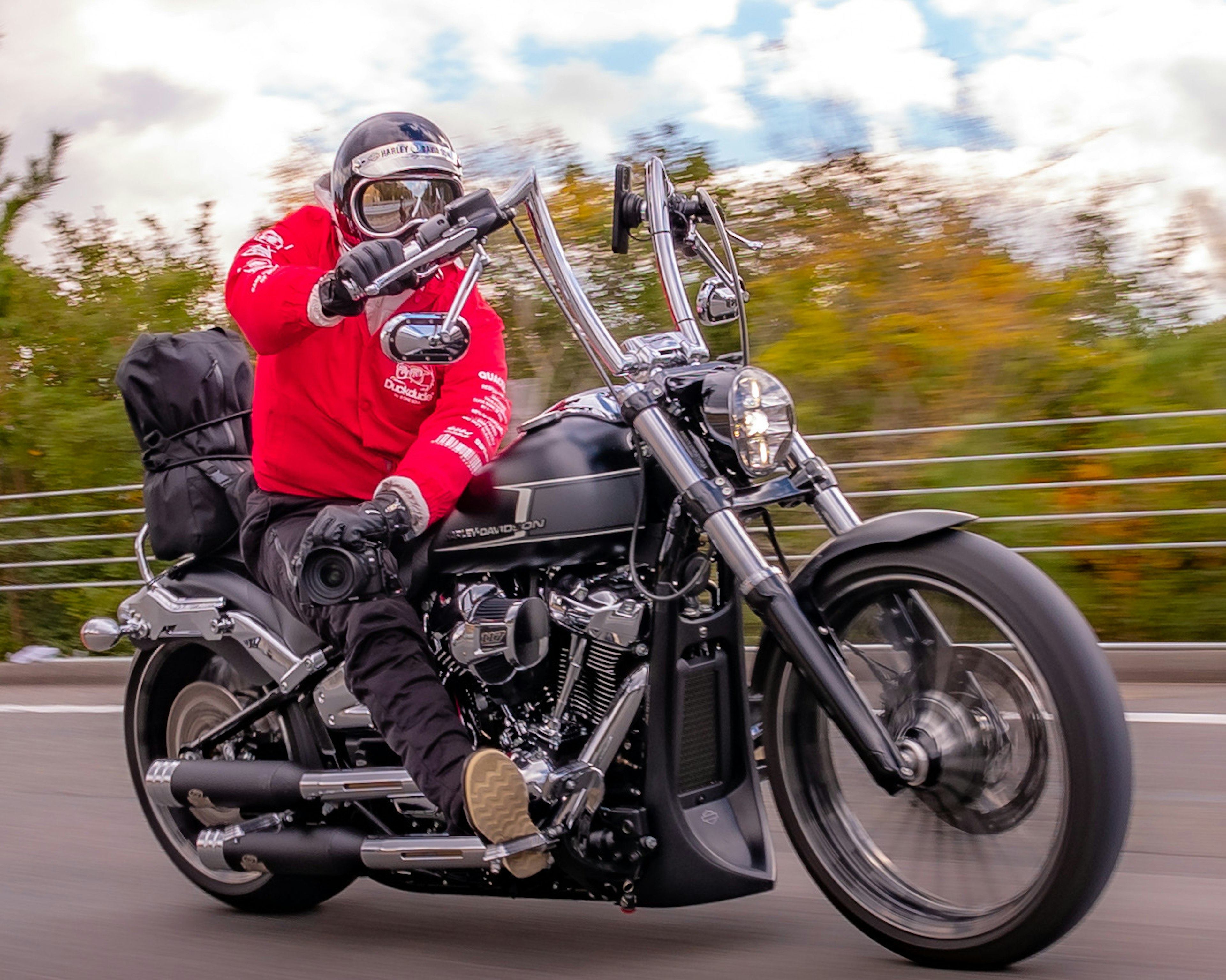 A rider in a red jacket riding a motorcycle on a scenic road