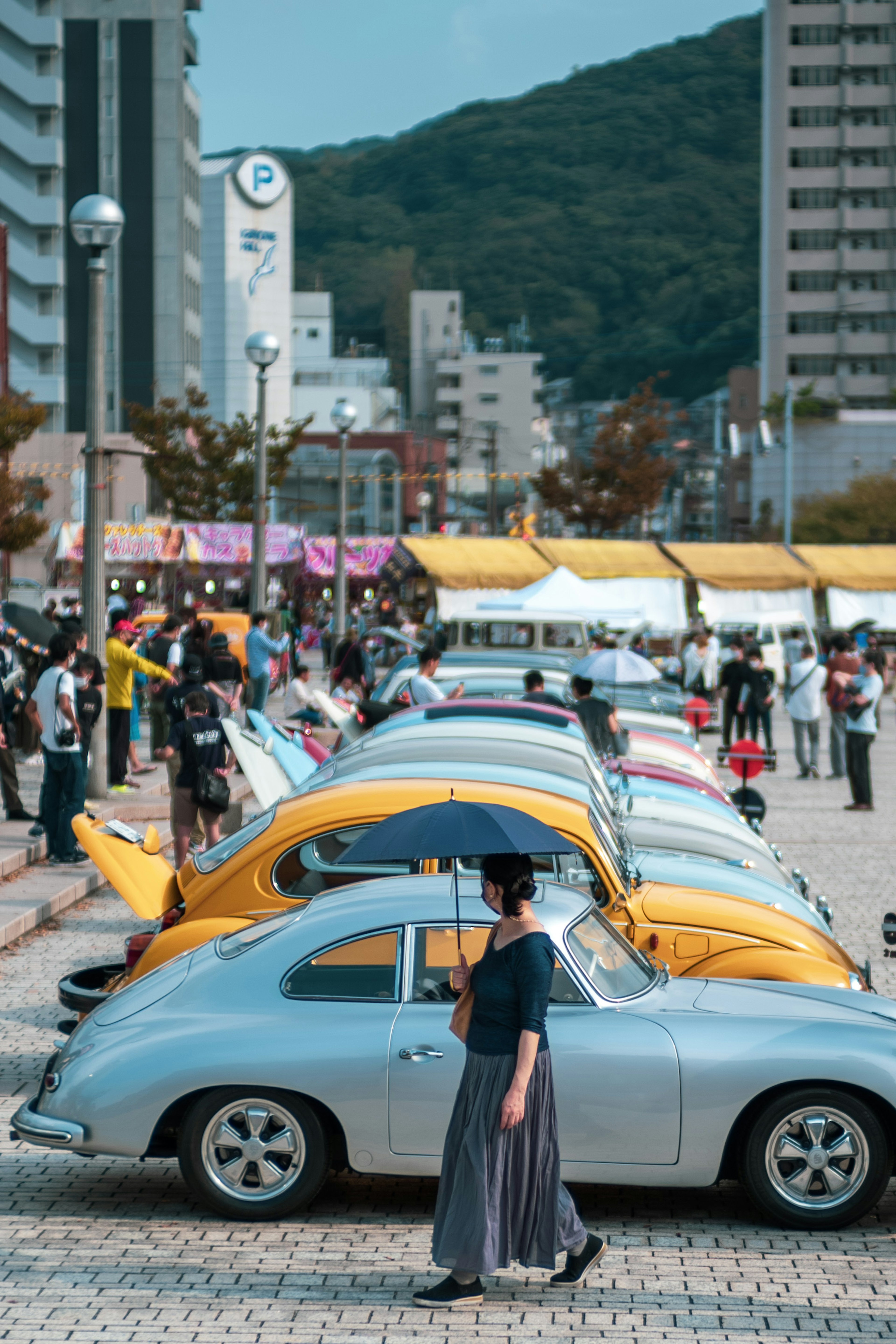 Una mujer caminando con un paraguas junto a coches vintage coloridos en un parque animado