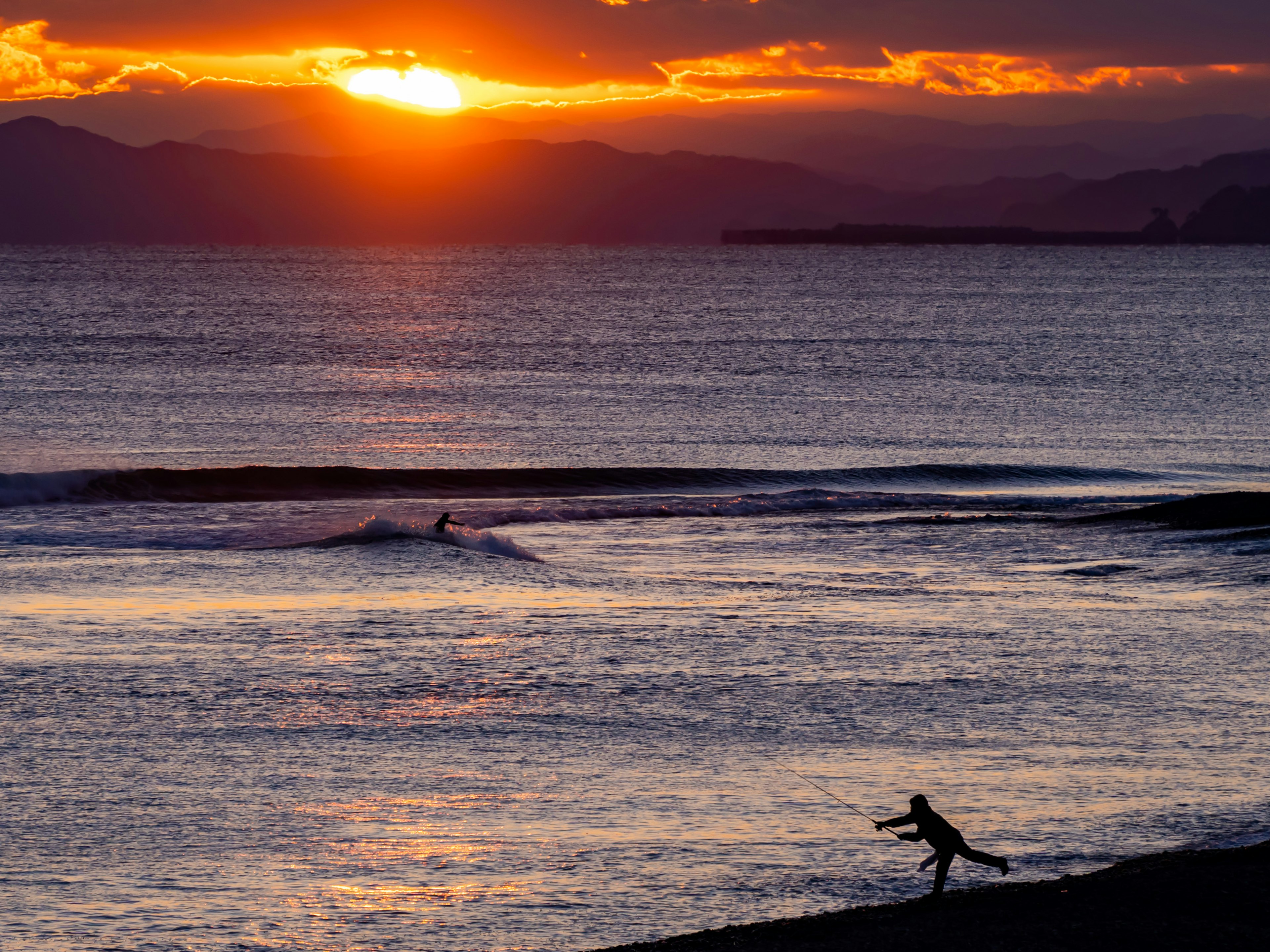 夕日が沈む海岸で遊ぶ人影と波