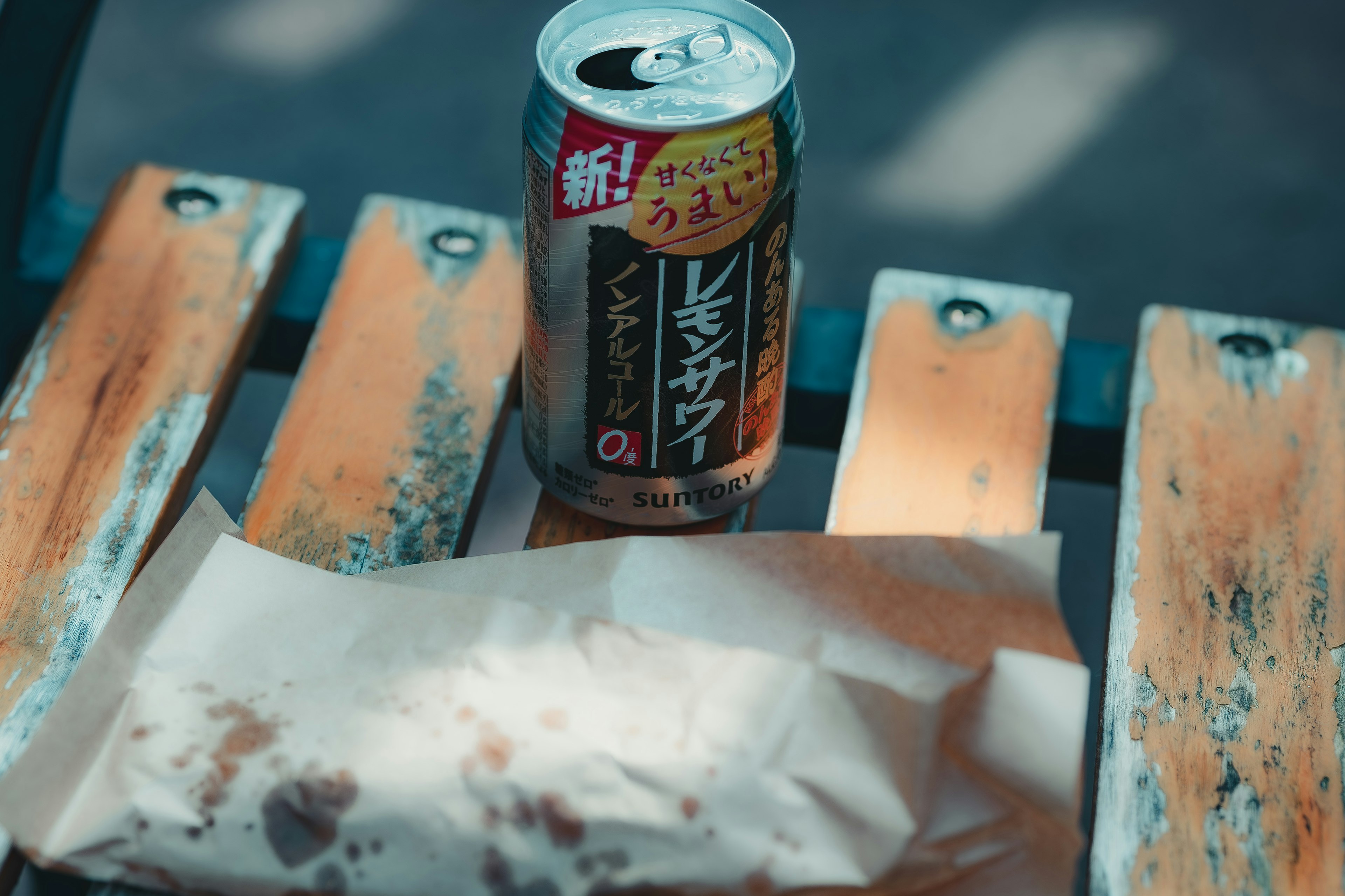 木のベンチの上に置かれた缶ビールと紙に包まれた食べ物